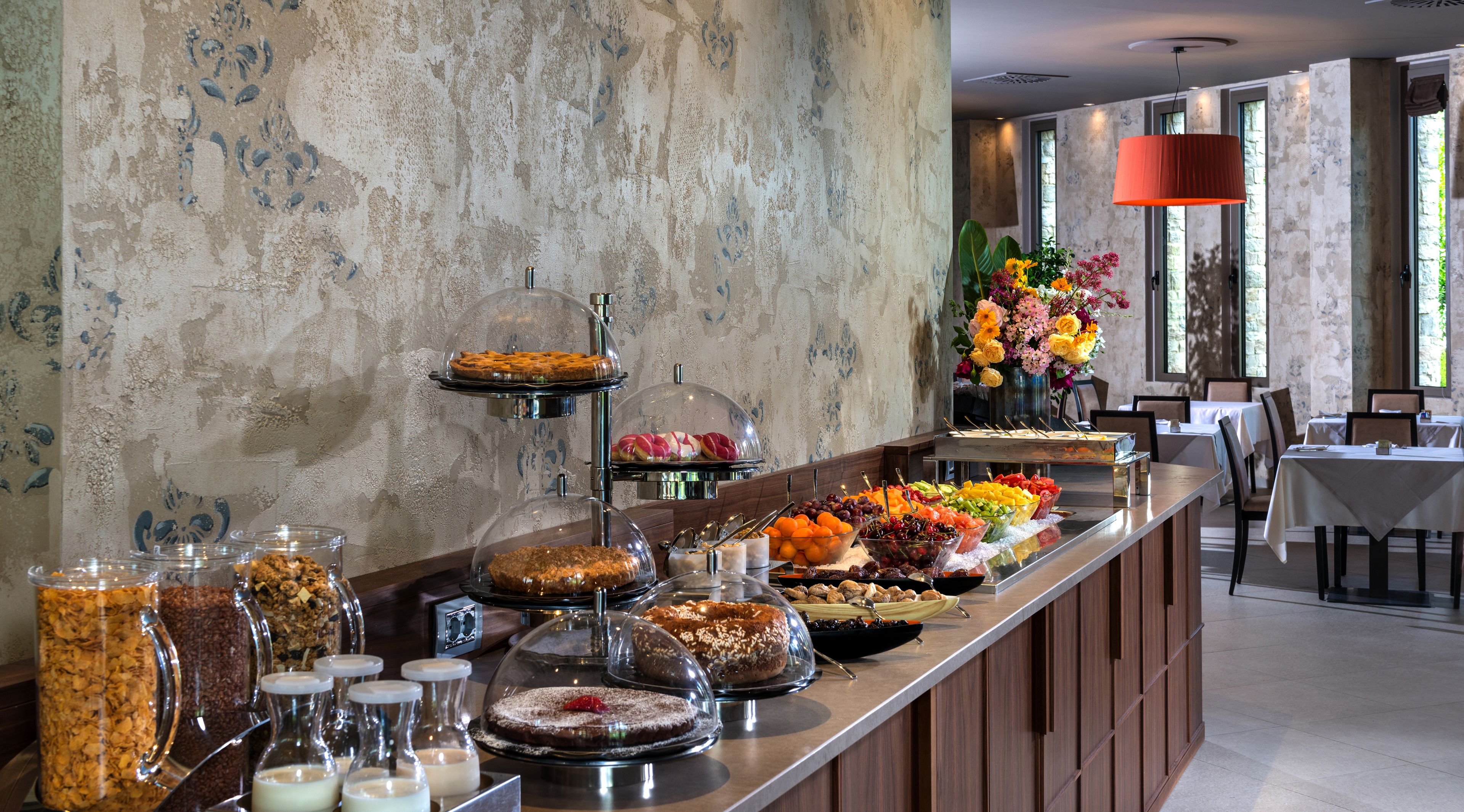 Een buffet met diverse gerechten, waaronder fruit, gebak en desserts, in een goed verlichte ruimte met een stenen muur en grote ramen.