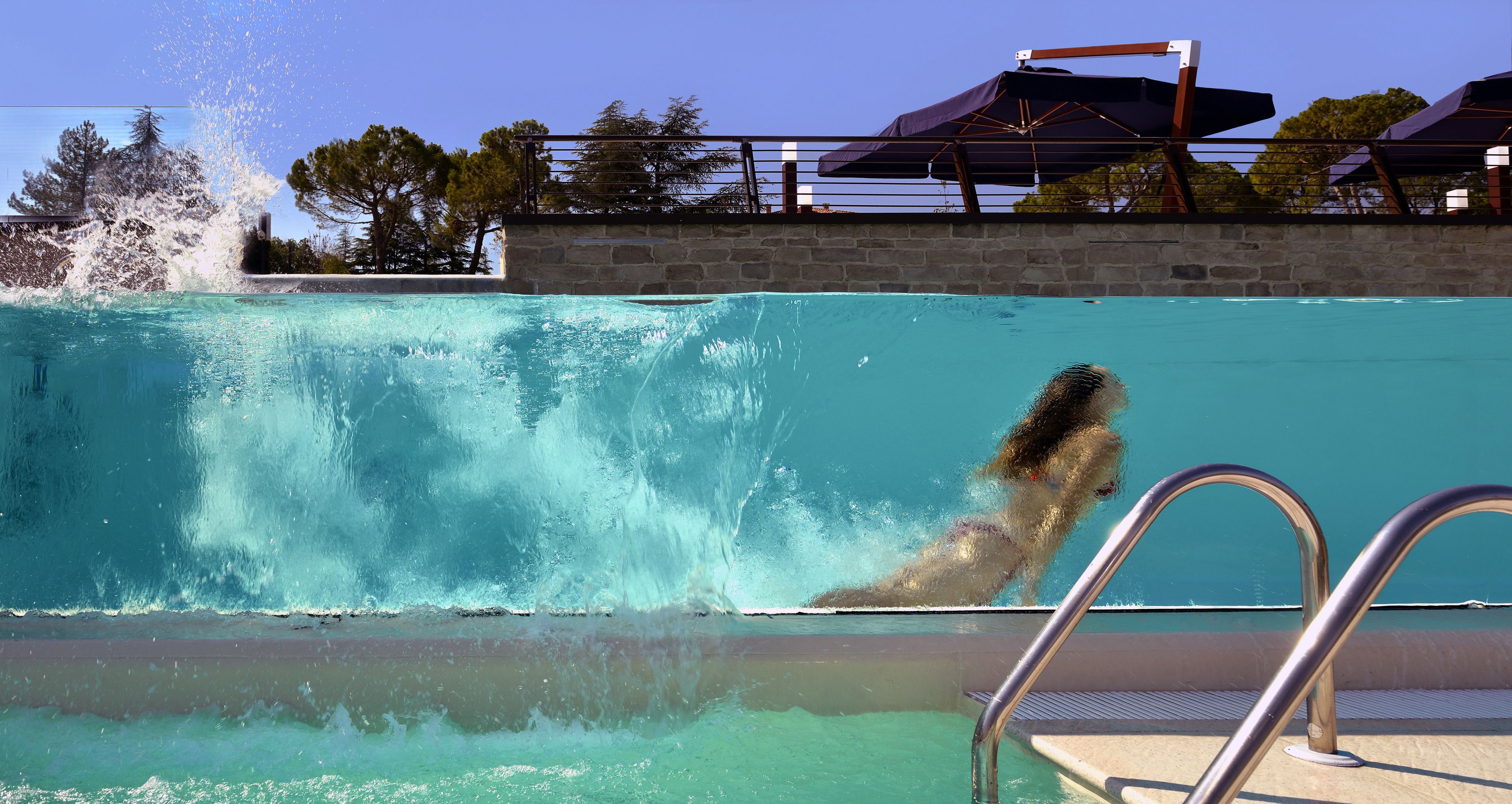 A swimming pool with a waterfall feature, a metal pool ladder, and a stone wall.