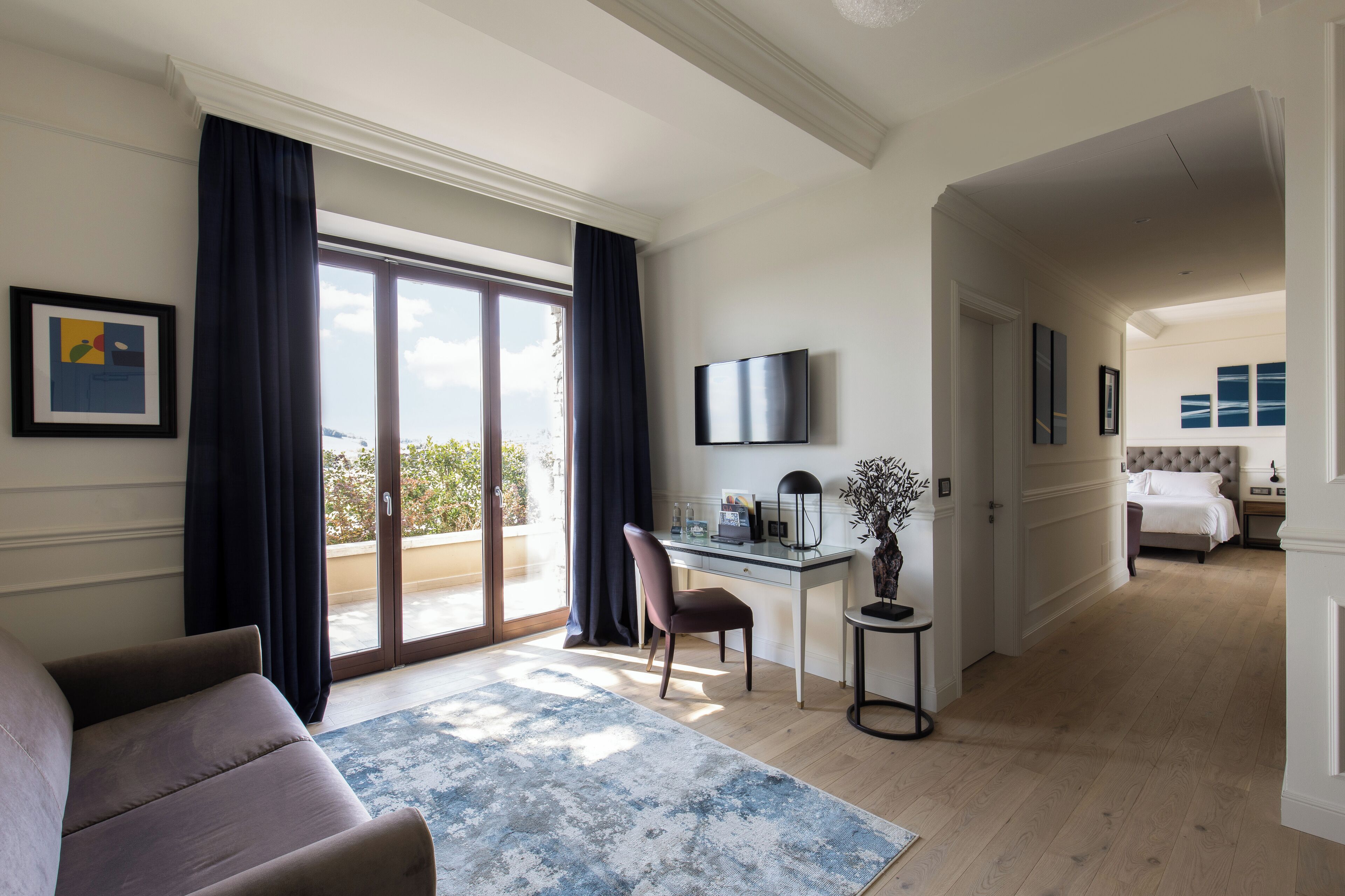 Une chambre d’hôtel dotée d’une grande porte-fenêtre coulissante donnant sur le balcon, d’un bureau avec une chaise, d’un téléviseur fixé au mur et d’un lit avec une tête de lit en arrière-plan.
