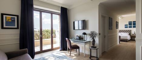 Une chambre d’hôtel dotée d’une grande porte-fenêtre coulissante donnant sur le balcon, d’un bureau avec une chaise, d’un téléviseur fixé au mur et d’un lit avec une tête de lit en arrière-plan.