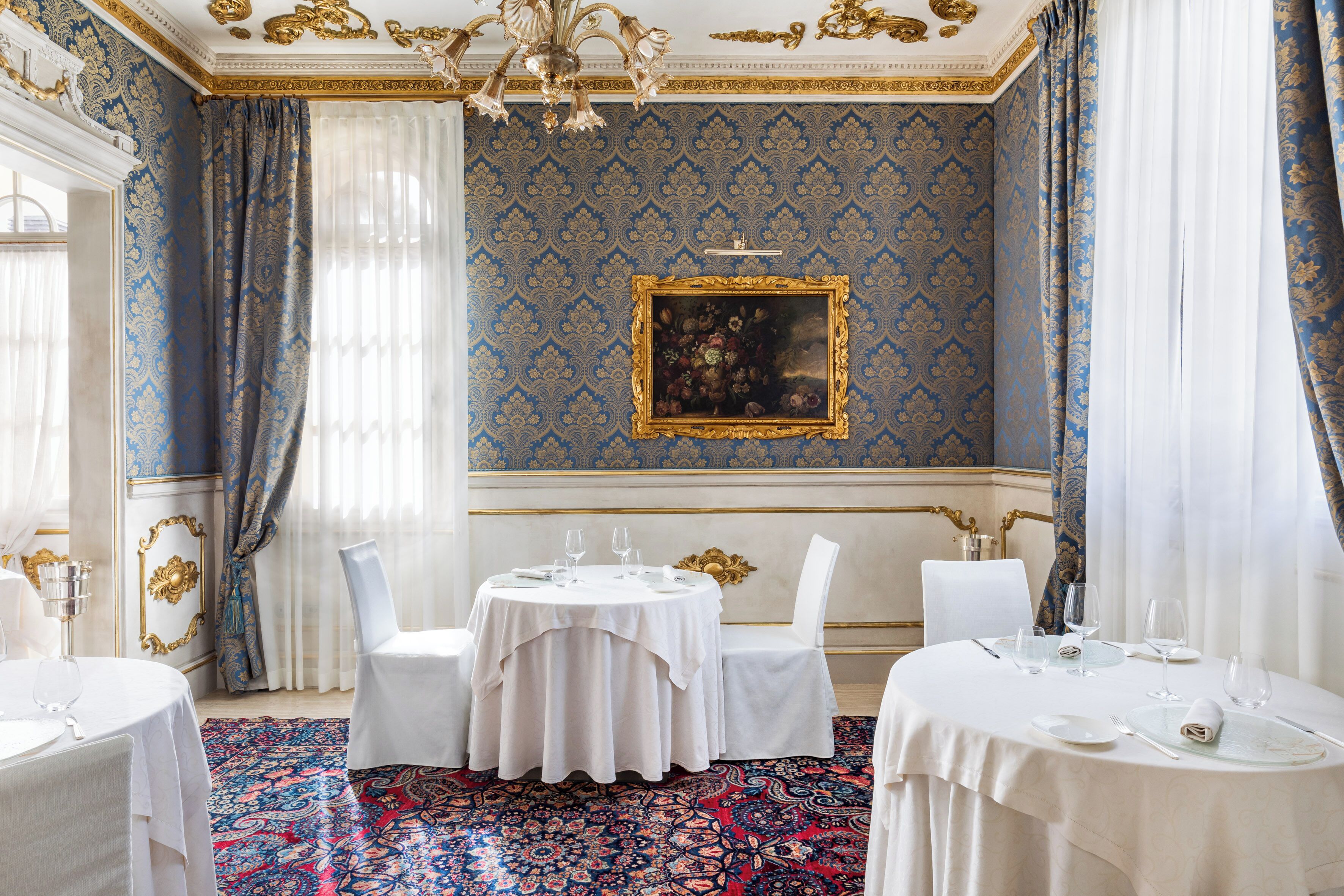 A dining room with ornate blue wallpaper, a chandelier, and a table set for two.