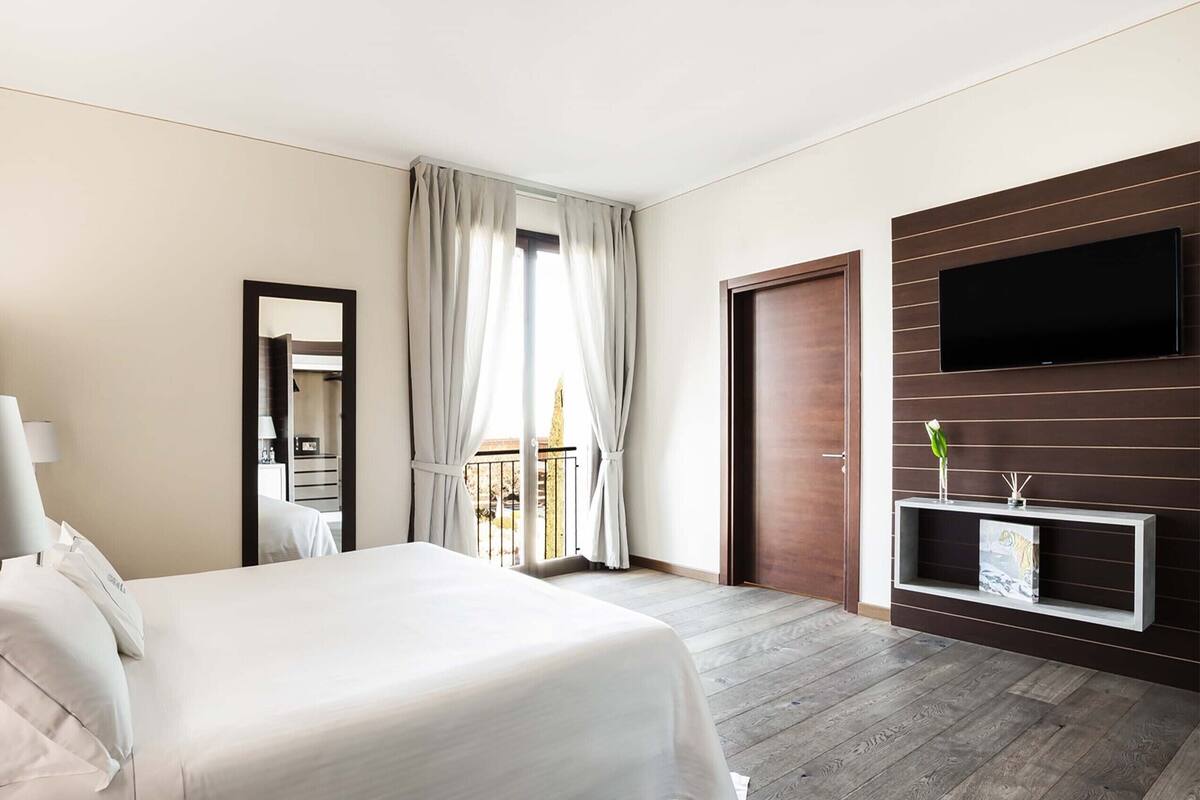 Ein Hotelzimmer mit Bett, Fernseher, Spiegel und einem Balkon mit Vorhängen.
