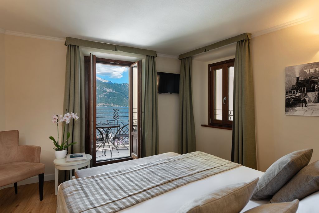 Habitación de hotel con cama, una silla, una mesita, ventana con cortinas y un cuadro en la pared.