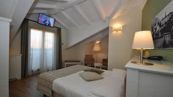 Habitación de hotel con una cama, un televisor instalado en el techo, un escritorio con lámpara y una silla.