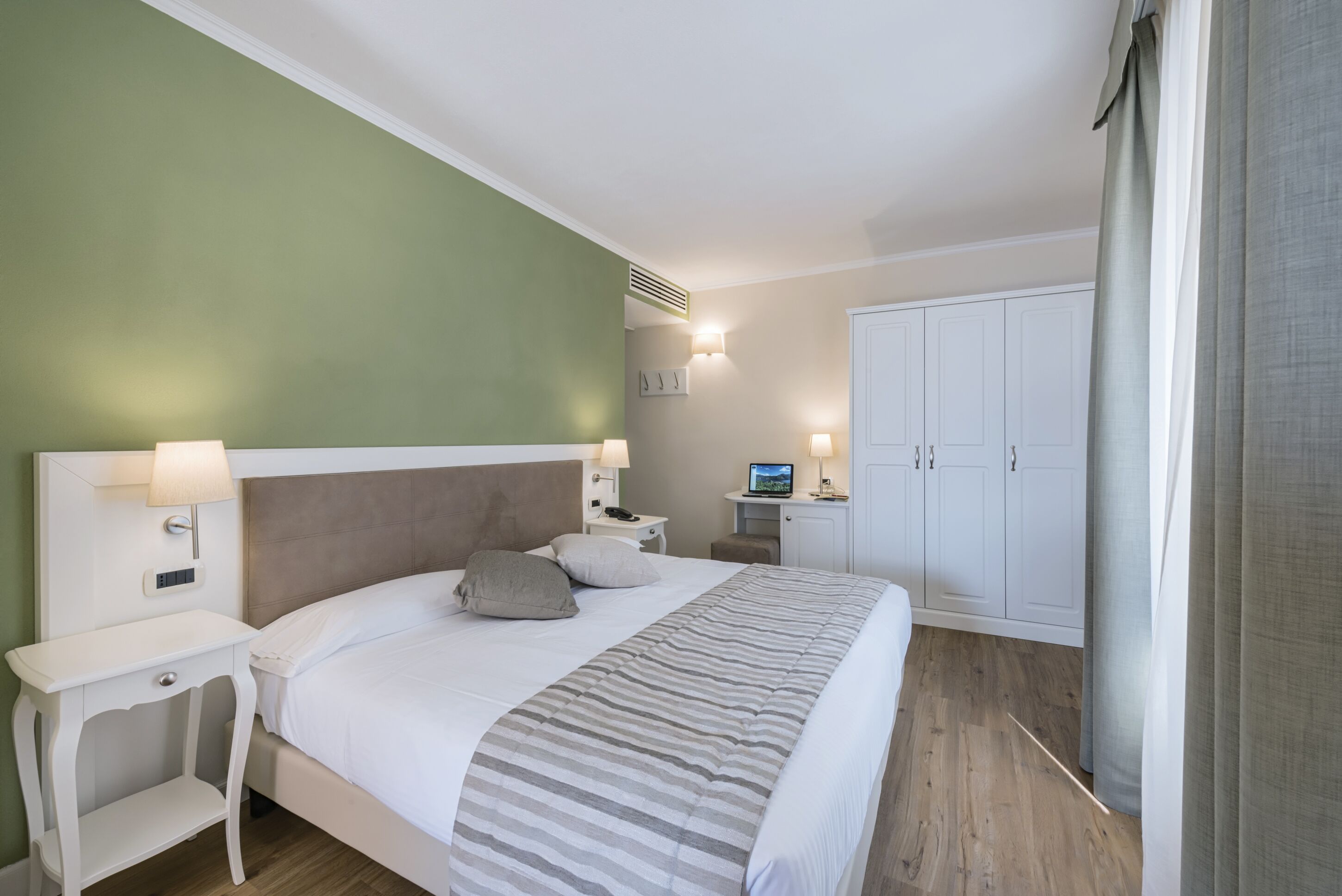 Een slaapkamer met een bed, nachtkastjes, een bureau en een kledingkast.