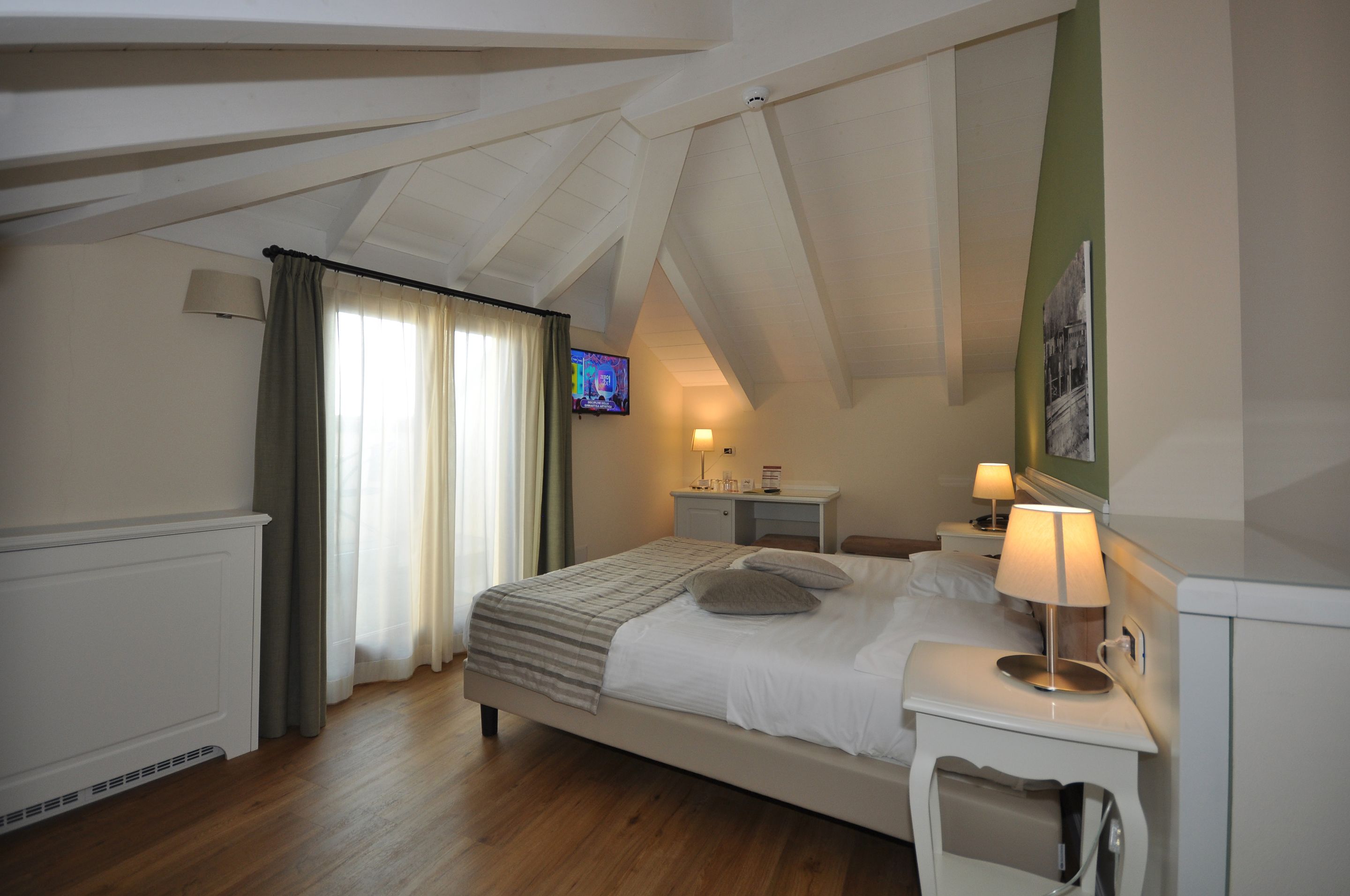 A hotel room with a bed, bedside tables, a TV, and a lamp.