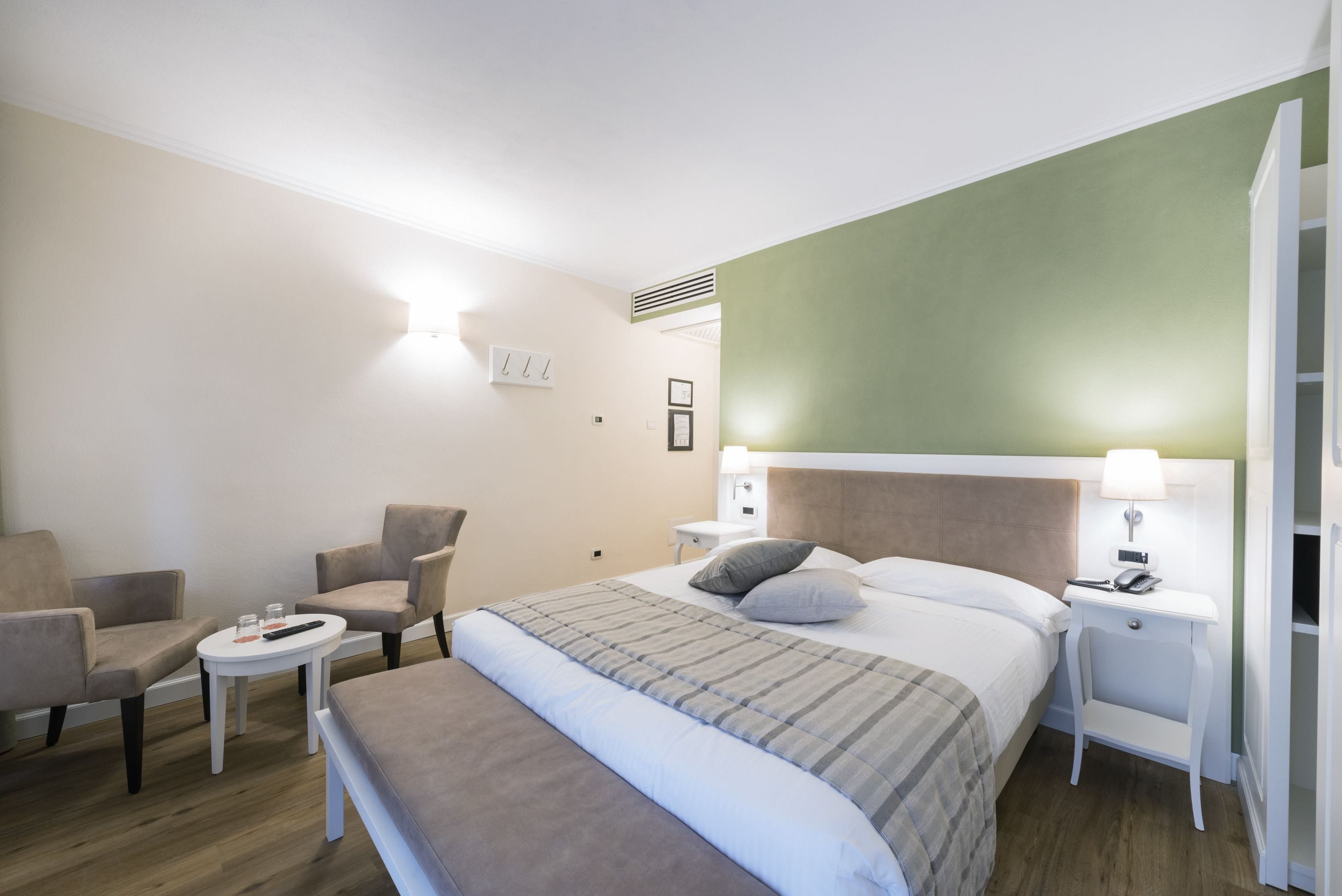 Una habitación de hotel con una cama, dos sillones, una mesita y una lámpara en la mesita de noche.