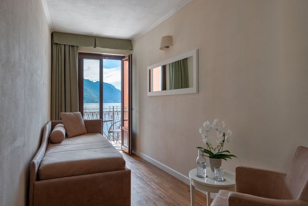 A hotel room with a balcony, a sofa, a chair, and a small table with a vase of flowers.