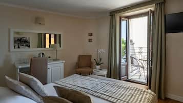 A hotel room with a bed, a desk, a chair, a small table with a lamp, and a balcony with a chair.