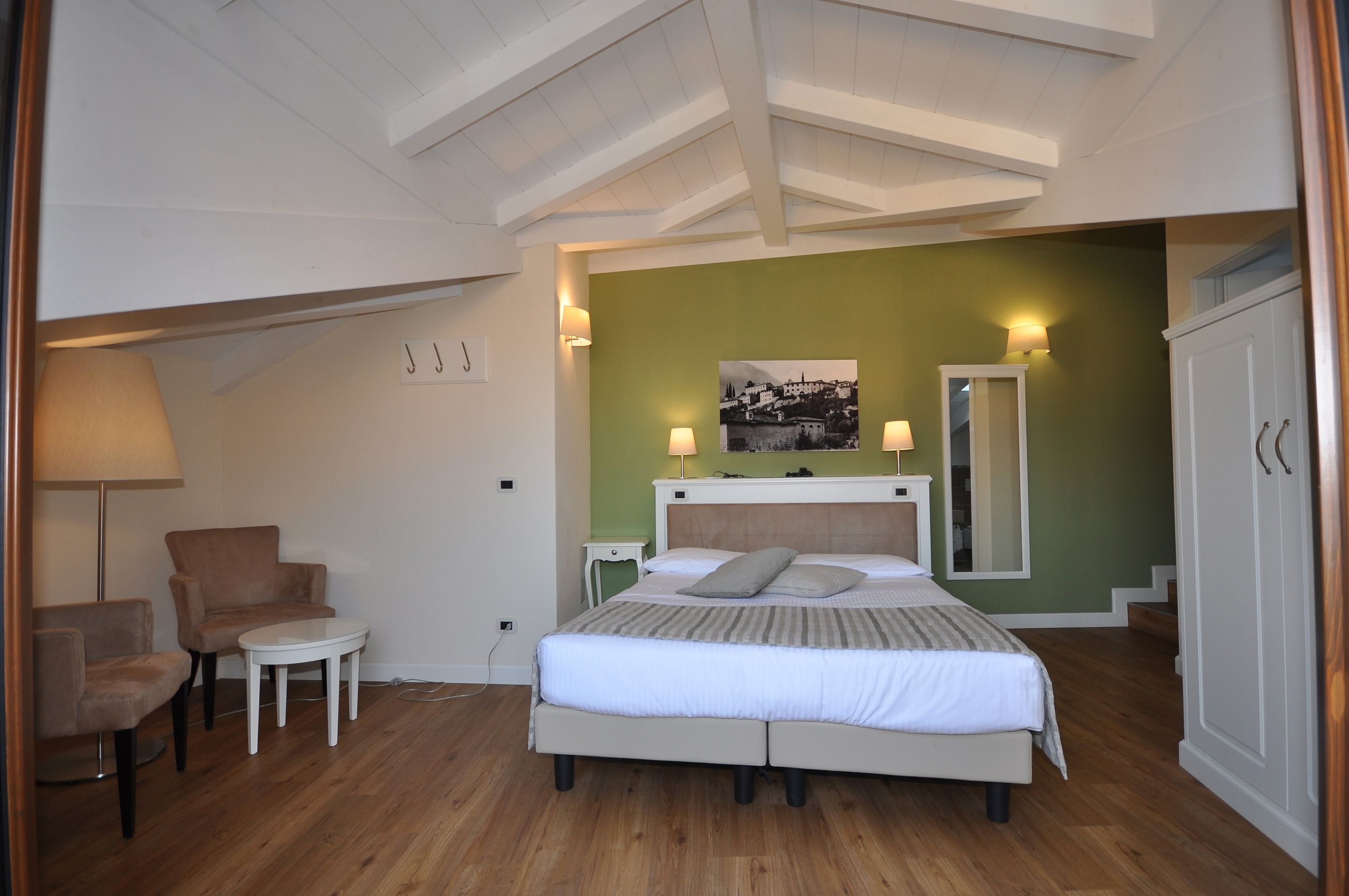 Ein Schlafzimmer mit einem Bett, zwei Stühlen, einem kleinen Tisch, einem Nachttisch und einem Spiegel.