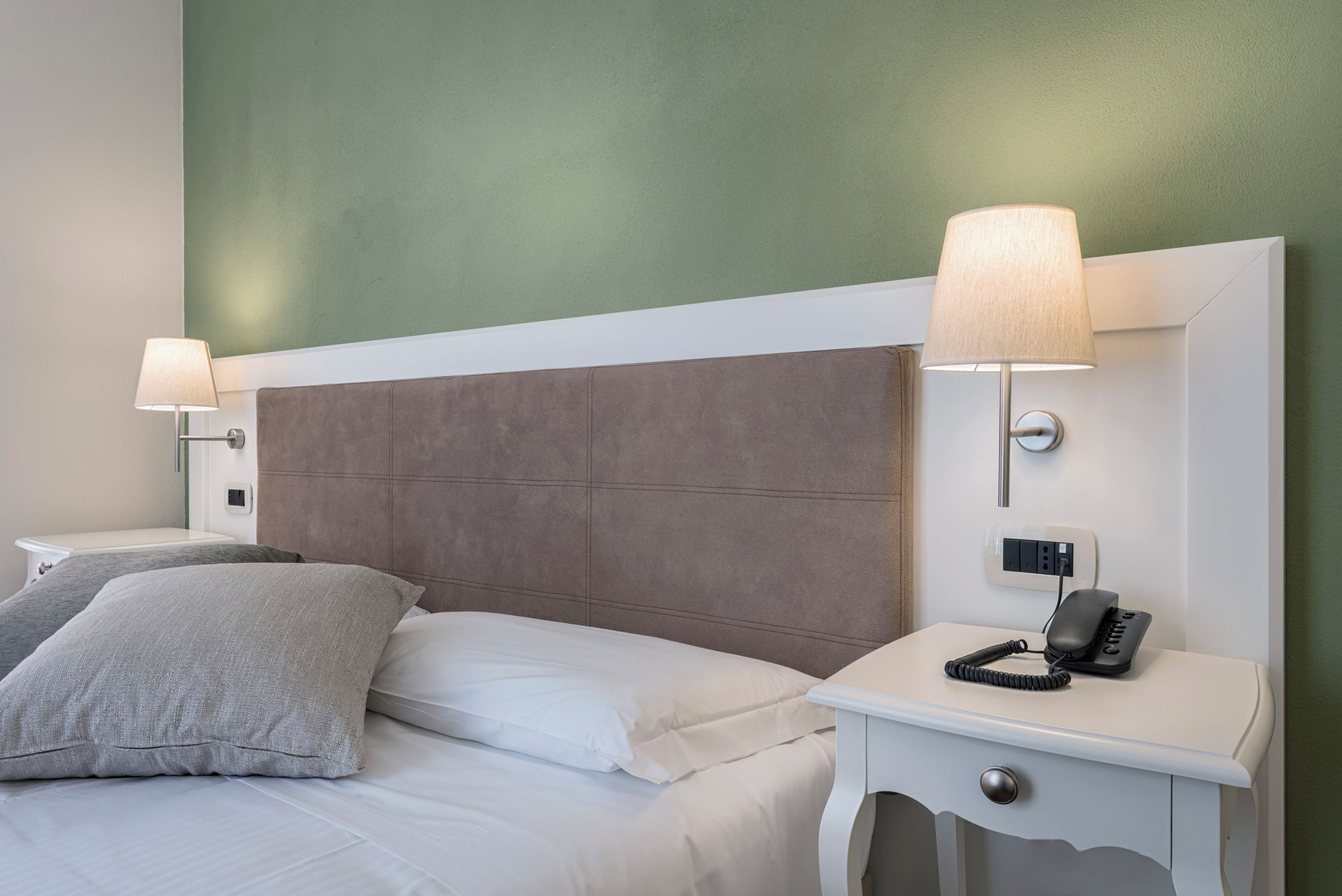Una habitación de hotel con una cama, dos lámparas de noche, un teléfono y un enchufe de pared.