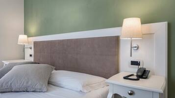 Una habitación de hotel con una cama, dos lámparas de noche, un teléfono y un enchufe de pared.