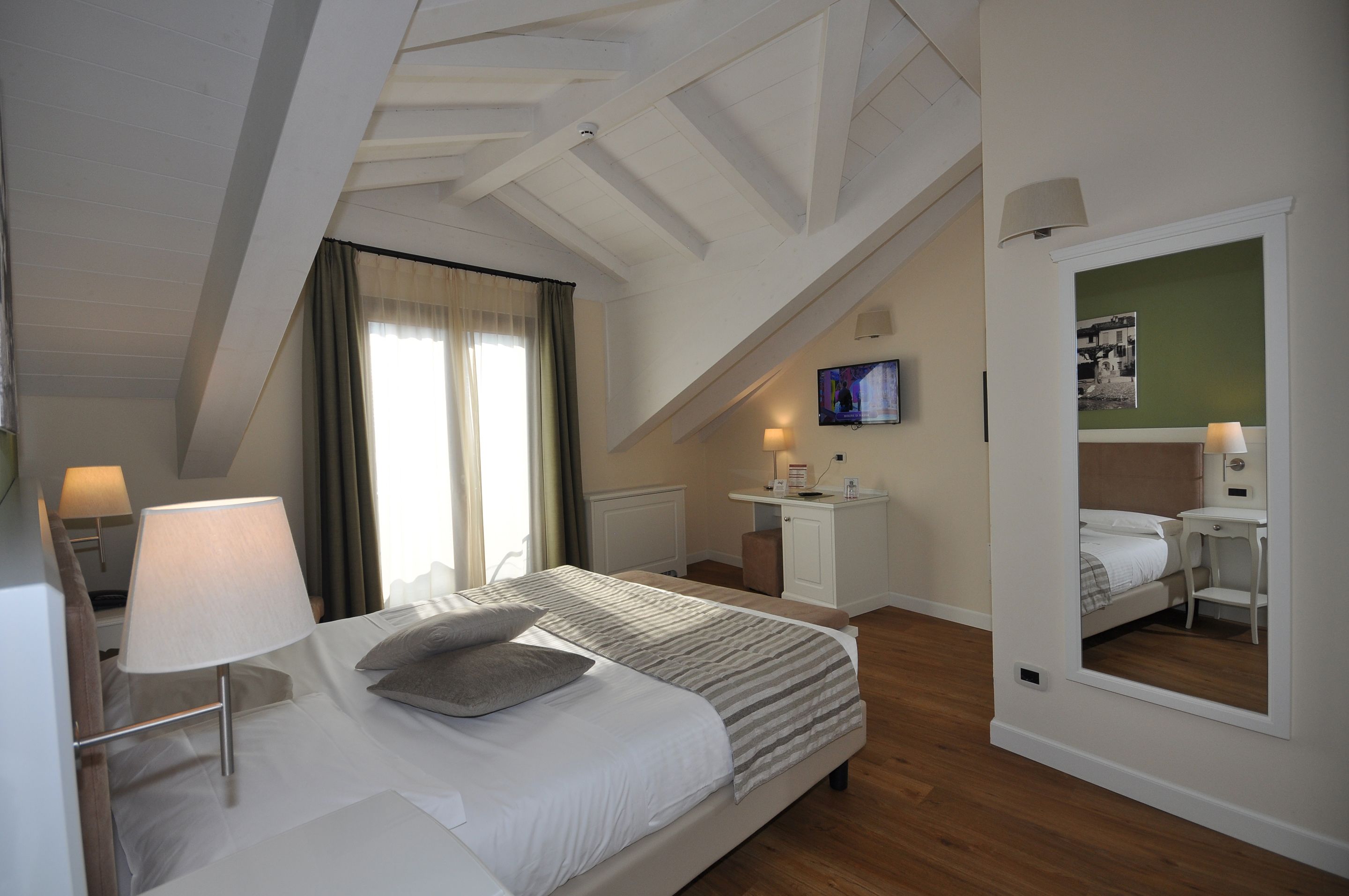 A hotel room with a bed, bedside table, lamp, and a TV on the wall.