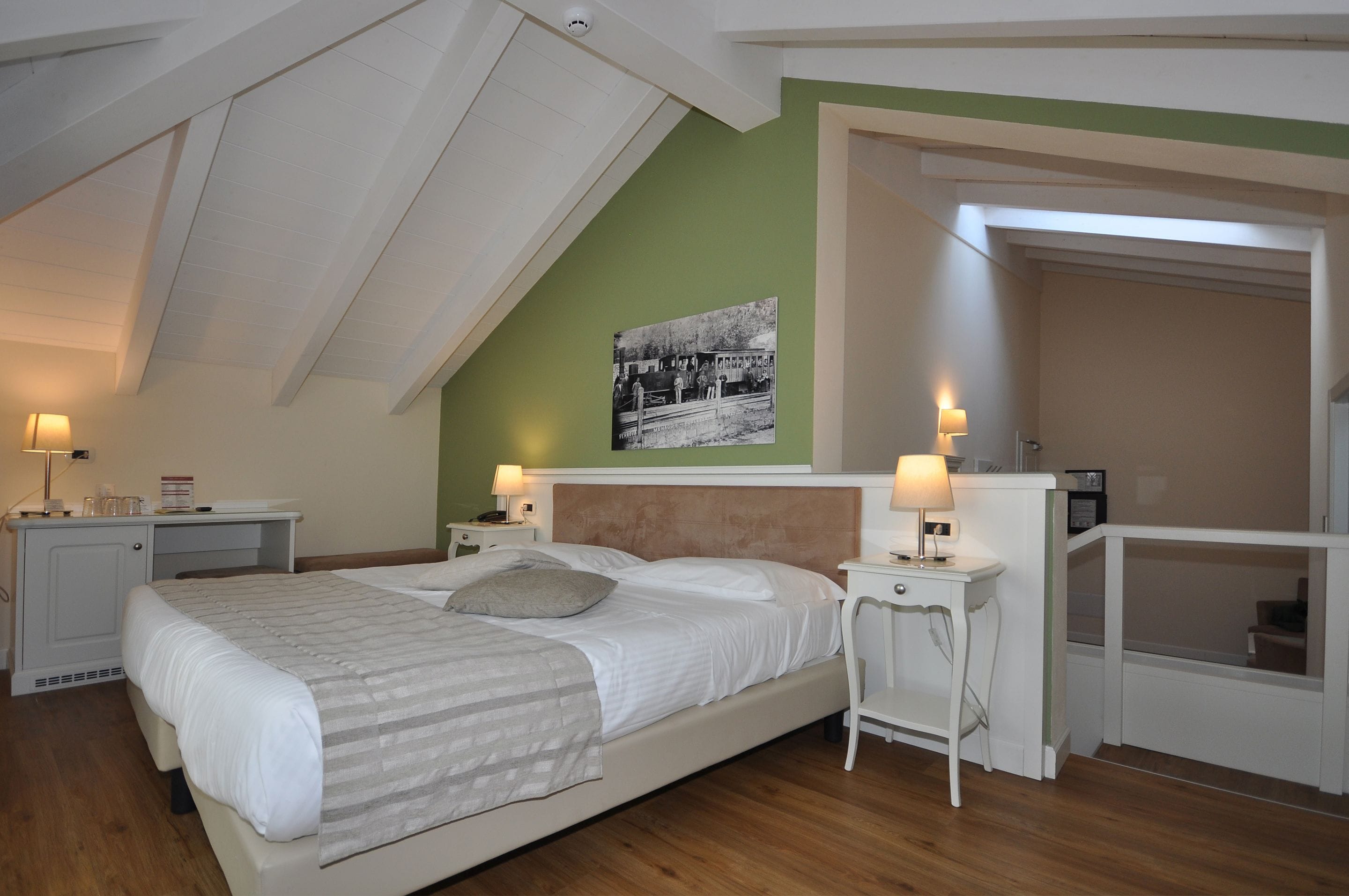 Une chambre à coucher comprenant un lit, des tables de chevet, une commode, une lampe, un tableau au mur et une porte donnant sur une autre pièce.