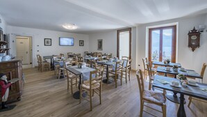 A dining area with multiple tables and chairs, a television, and a clock on the wall. - Hotel Garni Corona (Menaggio)