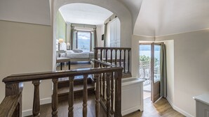 A spacious balcony with a wooden railing, a view of the sea, and a bedroom with a bed and a nightstand. - Hotel Garni Corona (Menaggio)