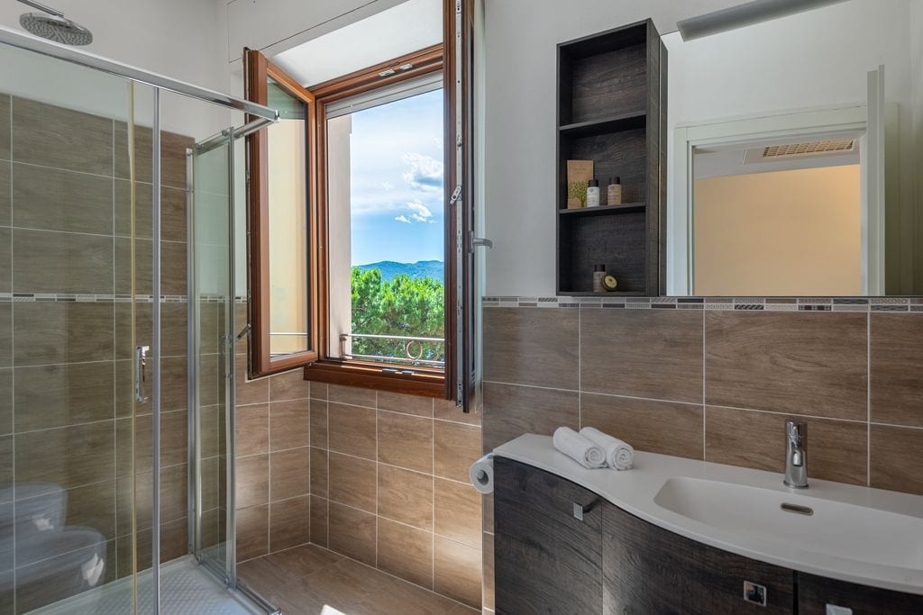 Une salle de bain avec une douche, un lavabo et une fenêtre donnant sur un espace verdoyant.