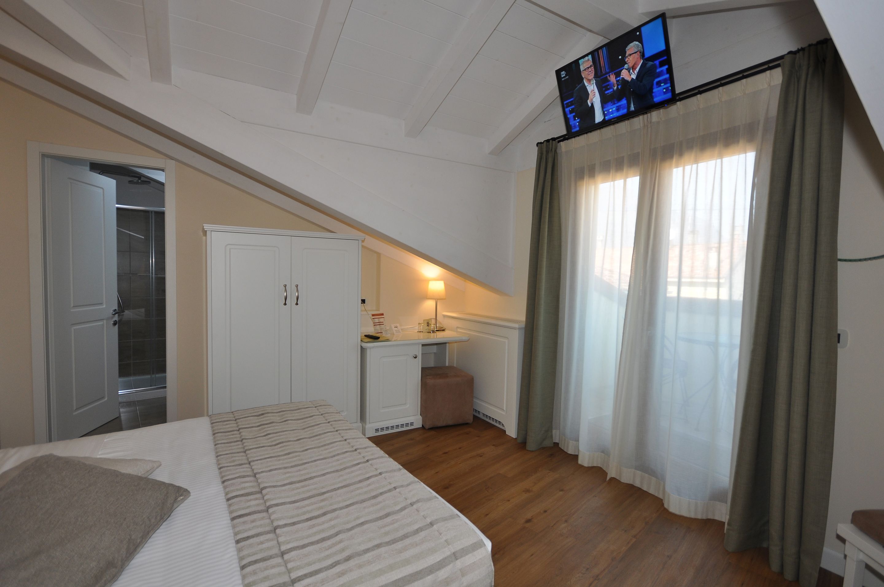 Een slaapkamer met een bed, een bureau, een spiegel, een kledingkast en een televisie aan de muur.