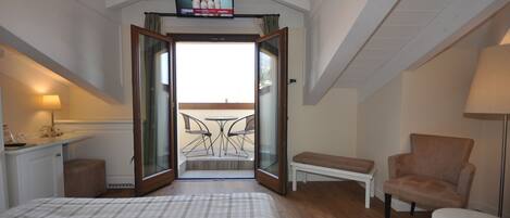Une chambre d’hôtel équipée d’un lit, d’un bureau, d’une chaise, d’un banc et d’un téléviseur fixé au plafond.