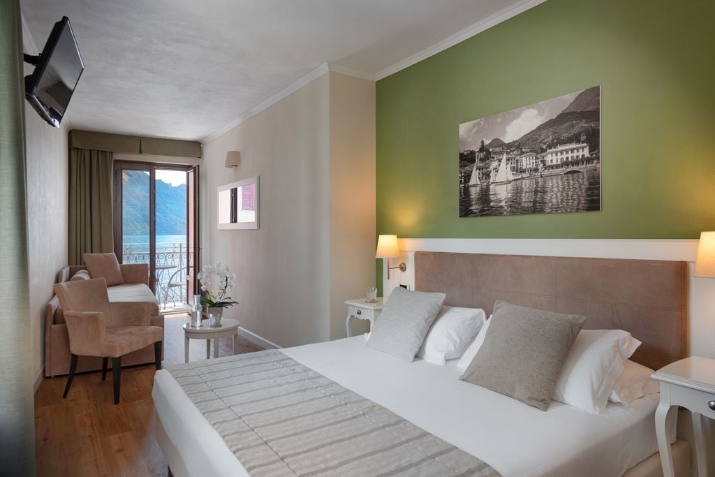 A hotel room with a bed, a chair, a small table, a TV, and a painting on the wall.