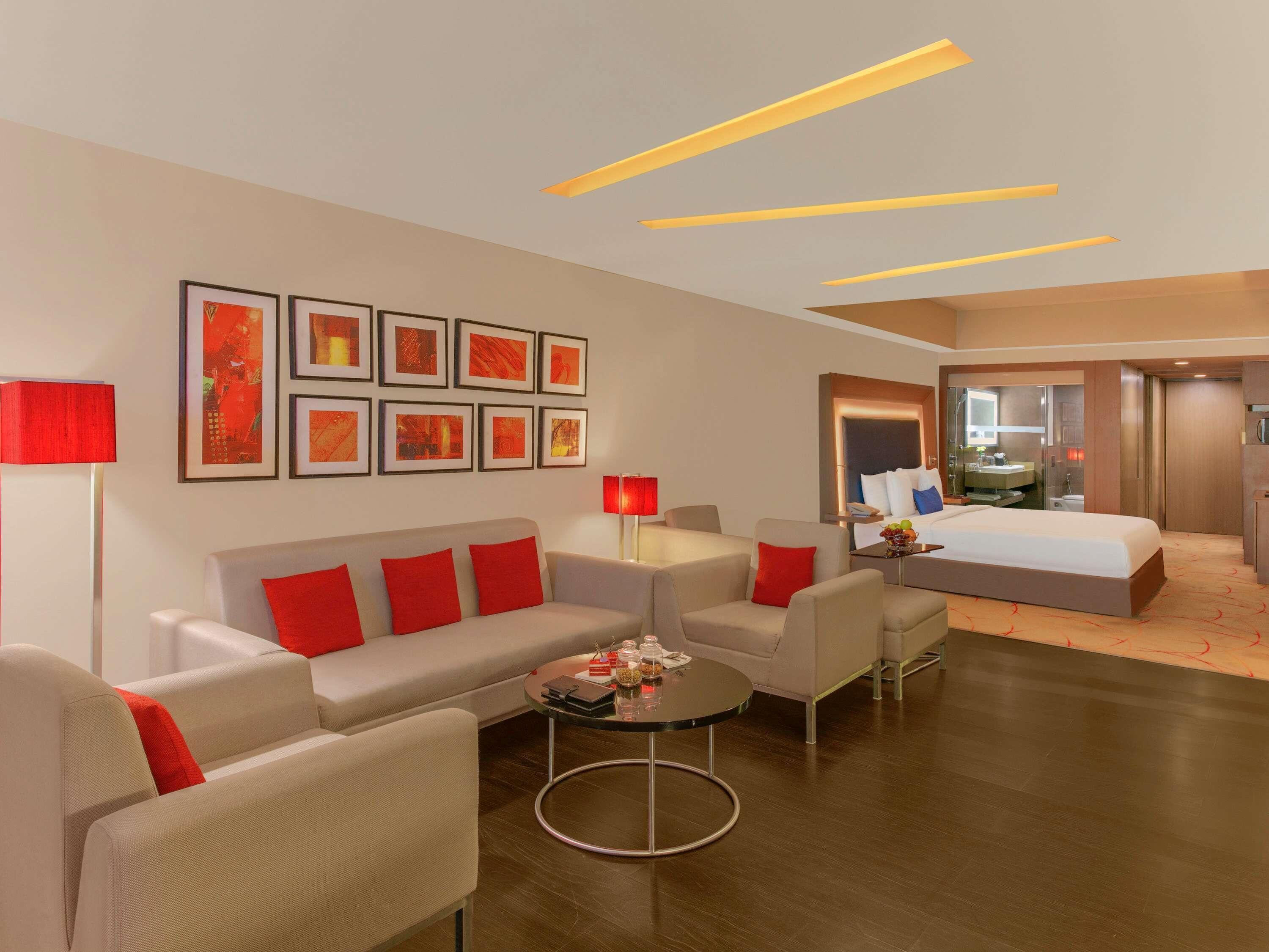 A modern hotel room with a sofa, armchairs, a round coffee table, and a bed.