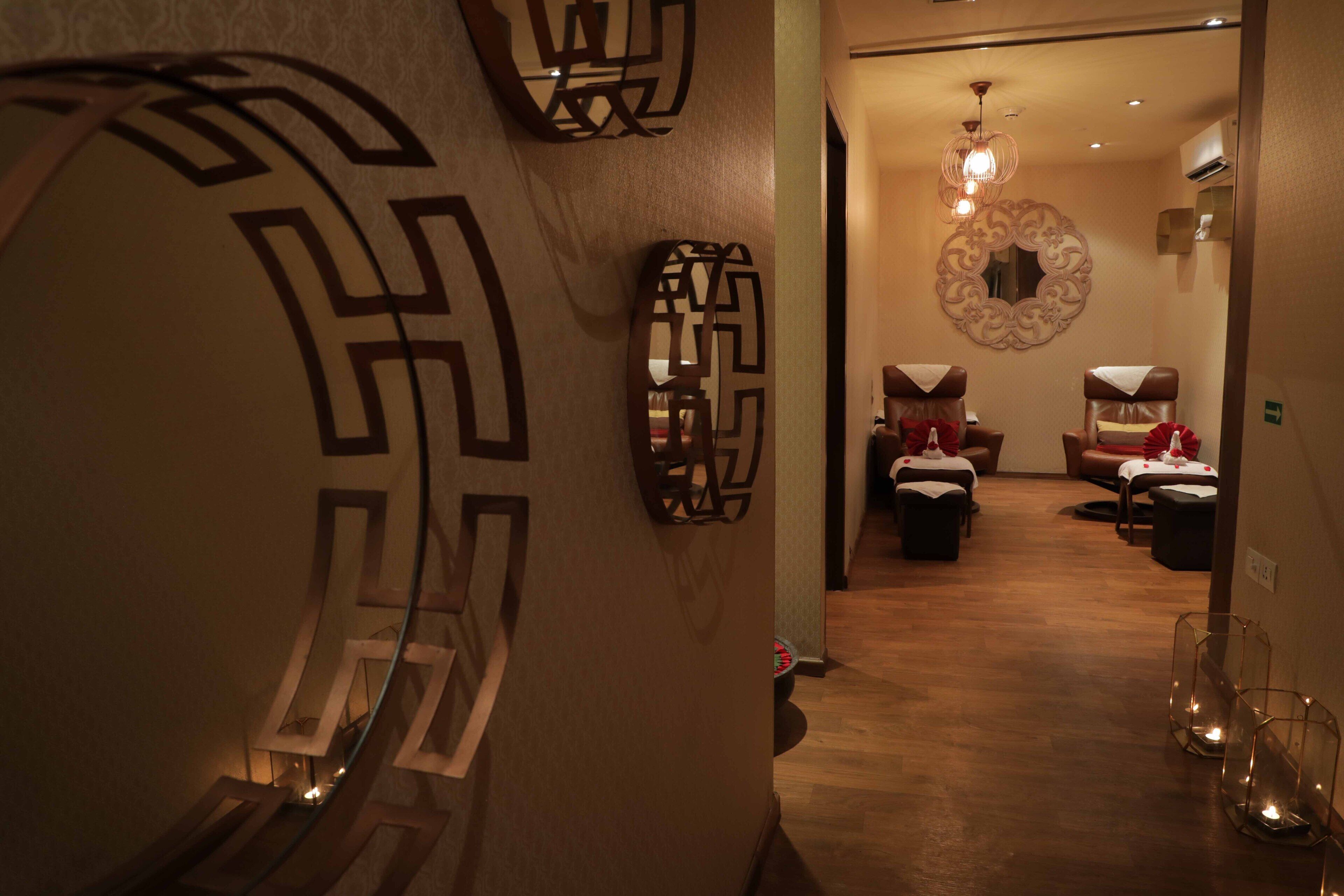 A hallway with decorative wall art, a wooden floor, and a seating area with a mirror and a chandelier.