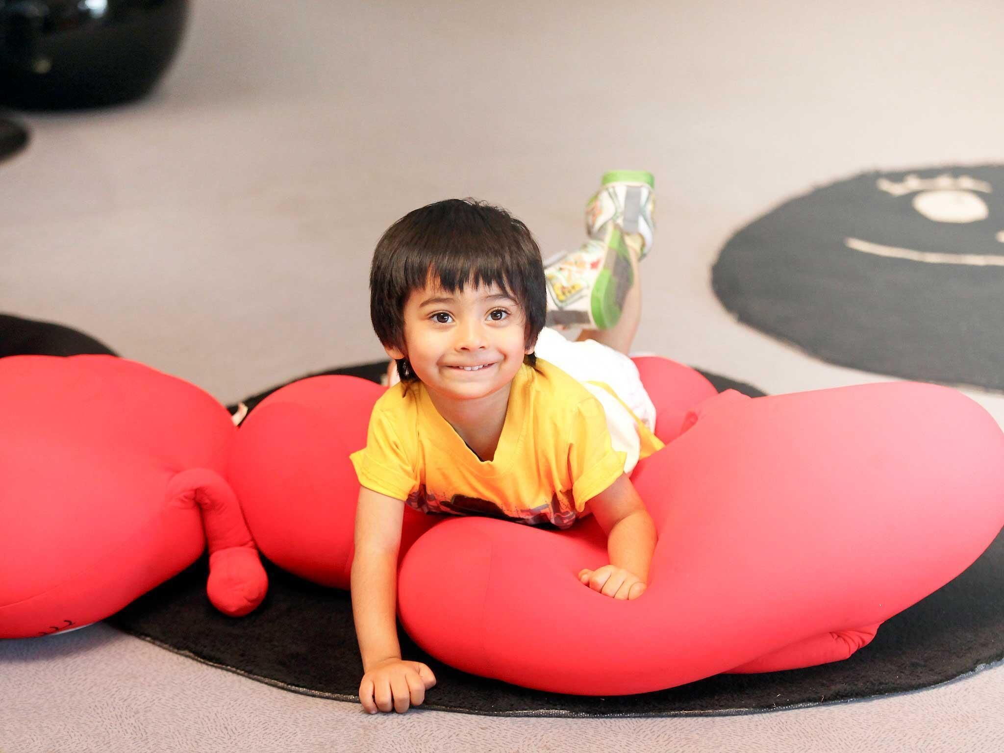 A child lying on a red cushion with a black mat in the background.