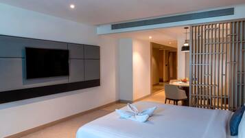 Une chambre d’hôtel moderne dotée d’un grand lit, d’un téléviseur à écran plat fixé au mur, d’un coin repas avec une table et des chaises, et d’une cloison décorative.