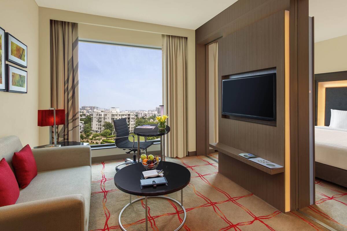 Une chambre d’hôtel avec un canapé, une petite table ronde ornée d’un vase de fleurs, un téléviseur à écran plat fixé au mur et un lit.