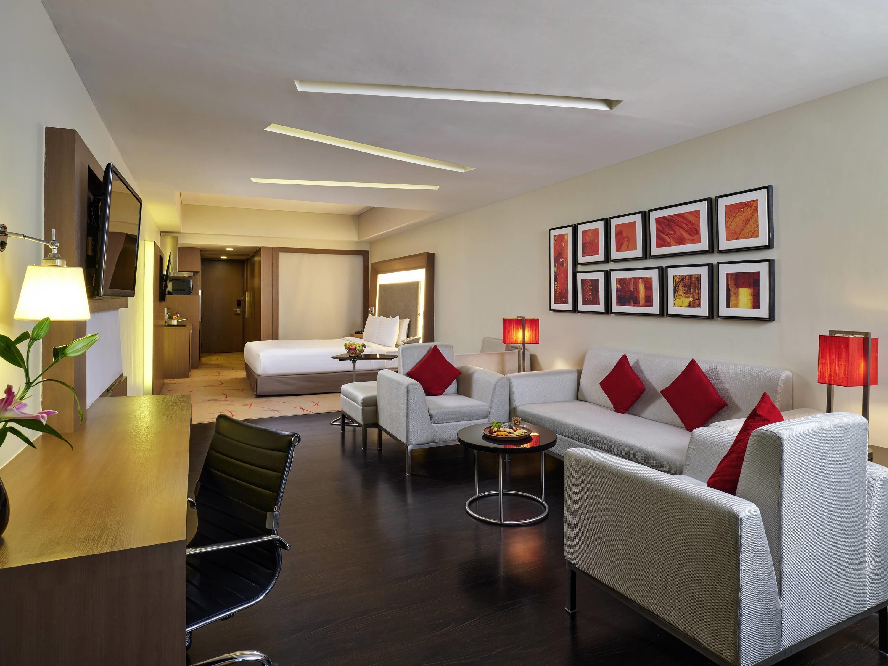 Une chambre d’hôtel comprenant un lit, deux canapés, un bureau, une chaise, une petite table et un mur décoré de tableaux.