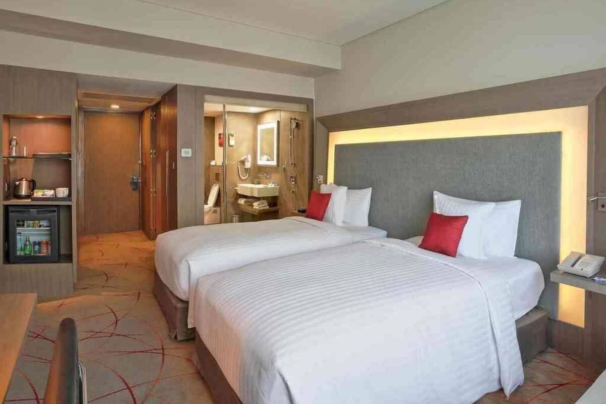 Une chambre d’hôtel avec deux lits, un bureau, un minibar et une salle de bain visible à travers une porte ouverte.