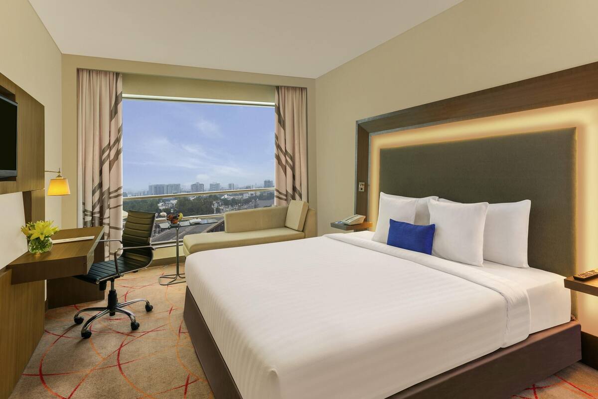 Une chambre d’hôtel avec un grand lit, un bureau avec une chaise, une télévision et une fenêtre avec des rideaux.