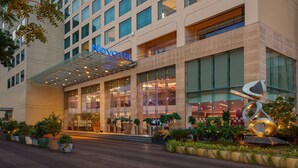 Un hotel moderno con fachada de vidrio, un llamativo letrero de 'NOVOTEL' y una escultura al frente.