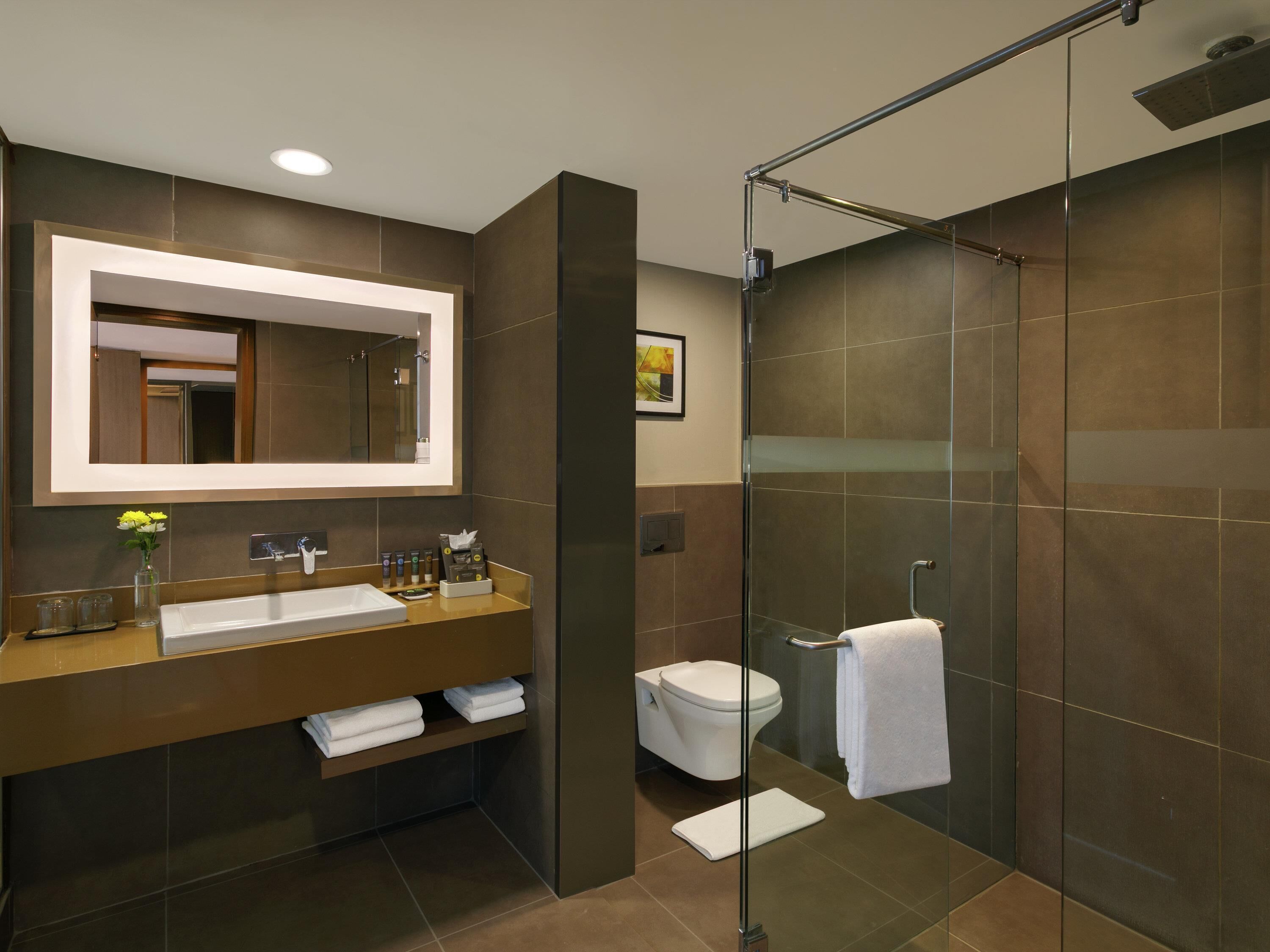 A modern bathroom with a large mirror, a glass-enclosed shower, and a vanity with a sink and towel rack.