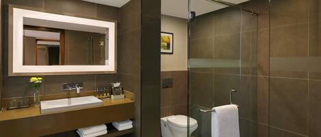 A modern bathroom with a large mirror, a glass-enclosed shower, and a vanity with a sink and towel rack.