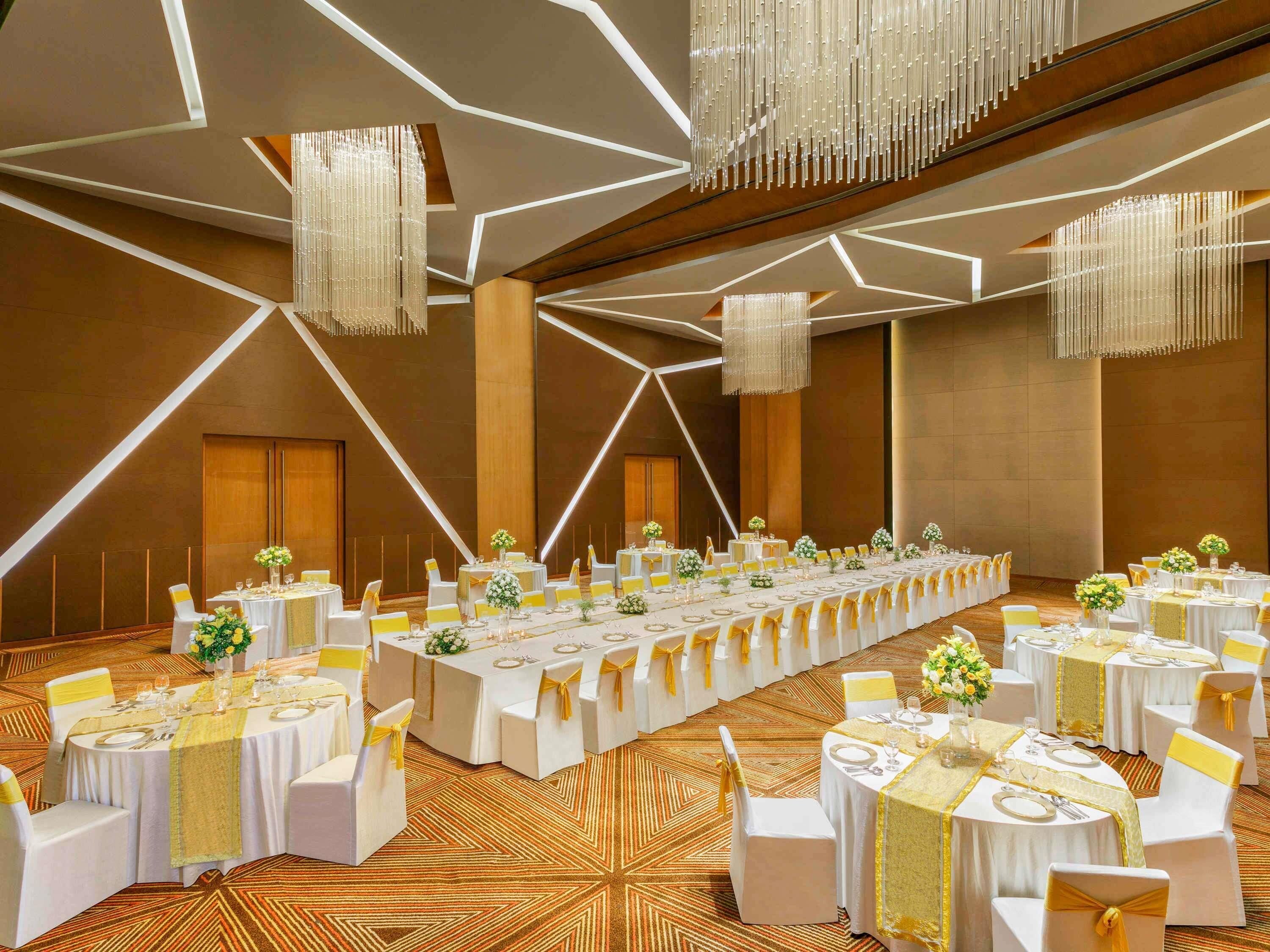 Un salón de banquetes con mesas largas, manteles blancos y fajas doradas.