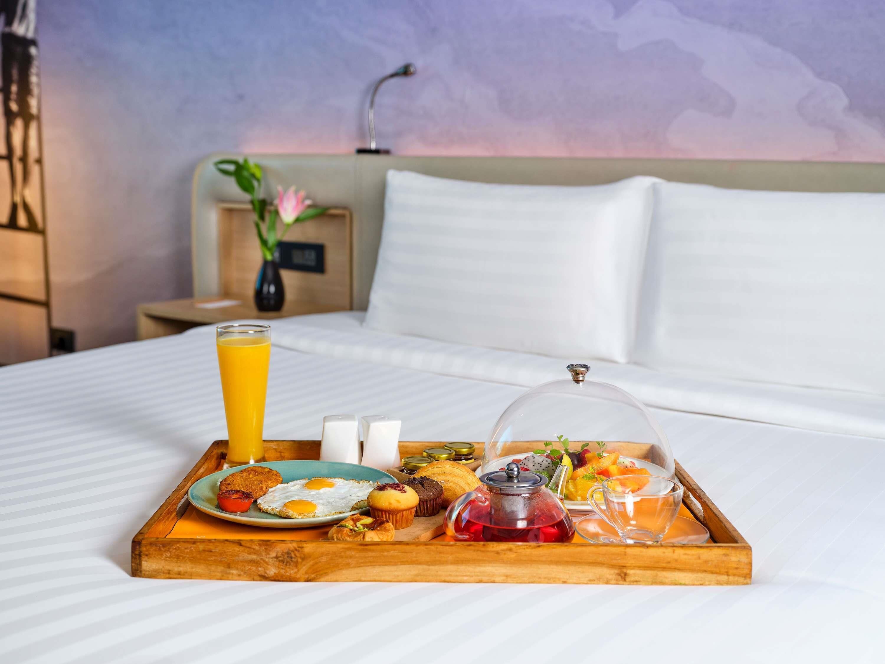 A breakfast tray with eggs, toast, muffins, and fruit on a bed in a hotel room.