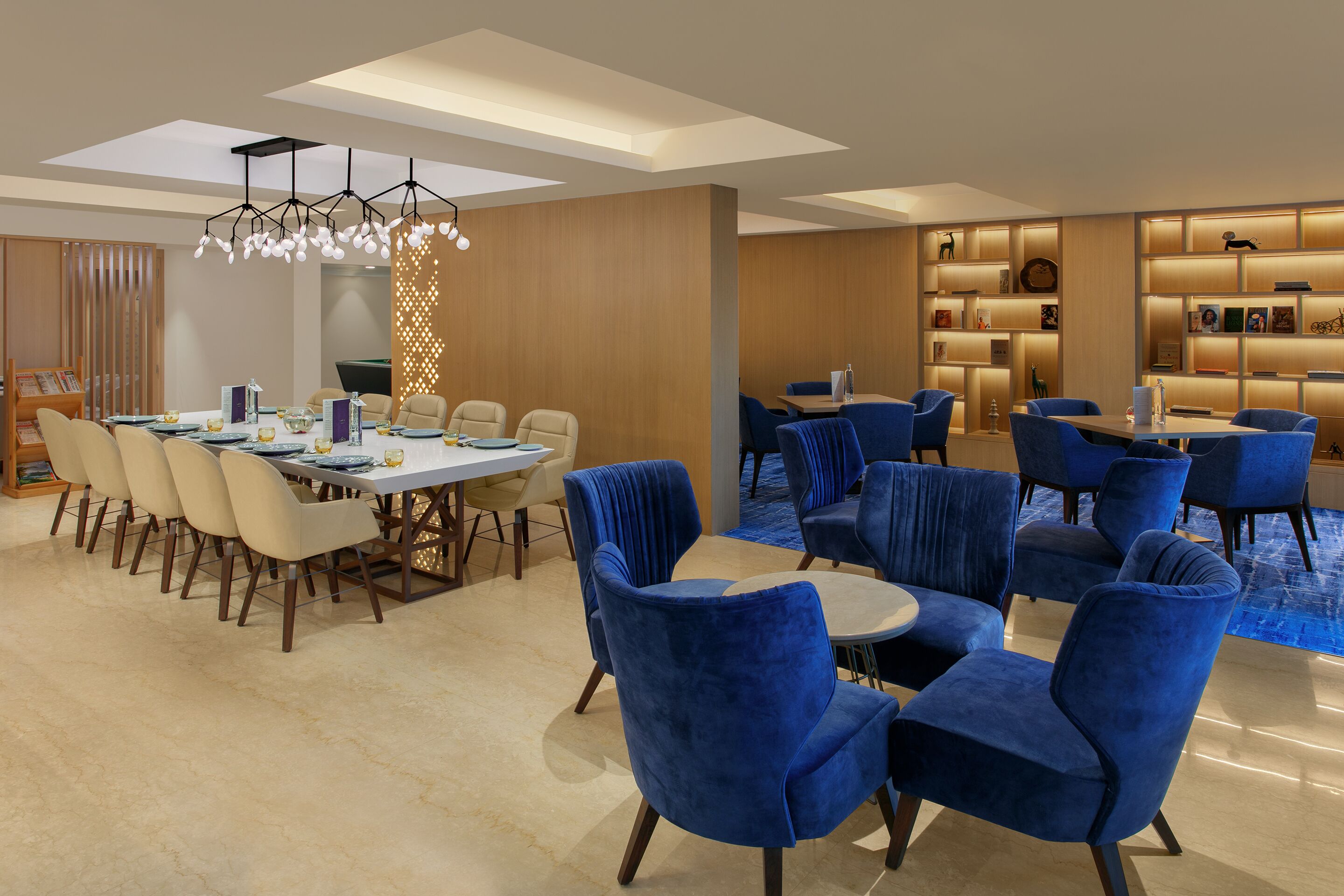 Un hall d’hôtel moderne comprenant un espace repas, des coins salon et un comptoir d’accueil bien éclairé.