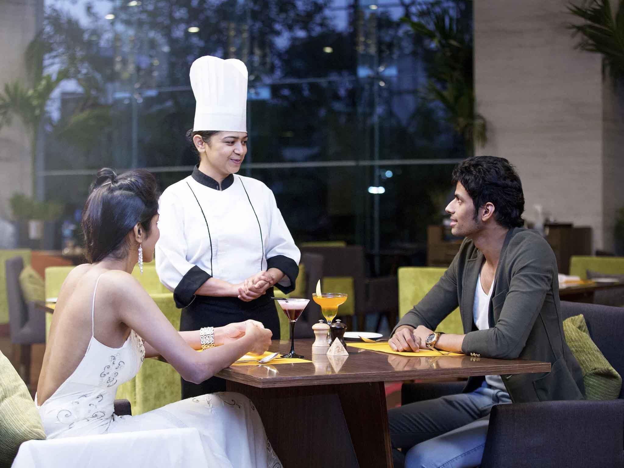 A dining area with a chef standing by a table where two people are seated.