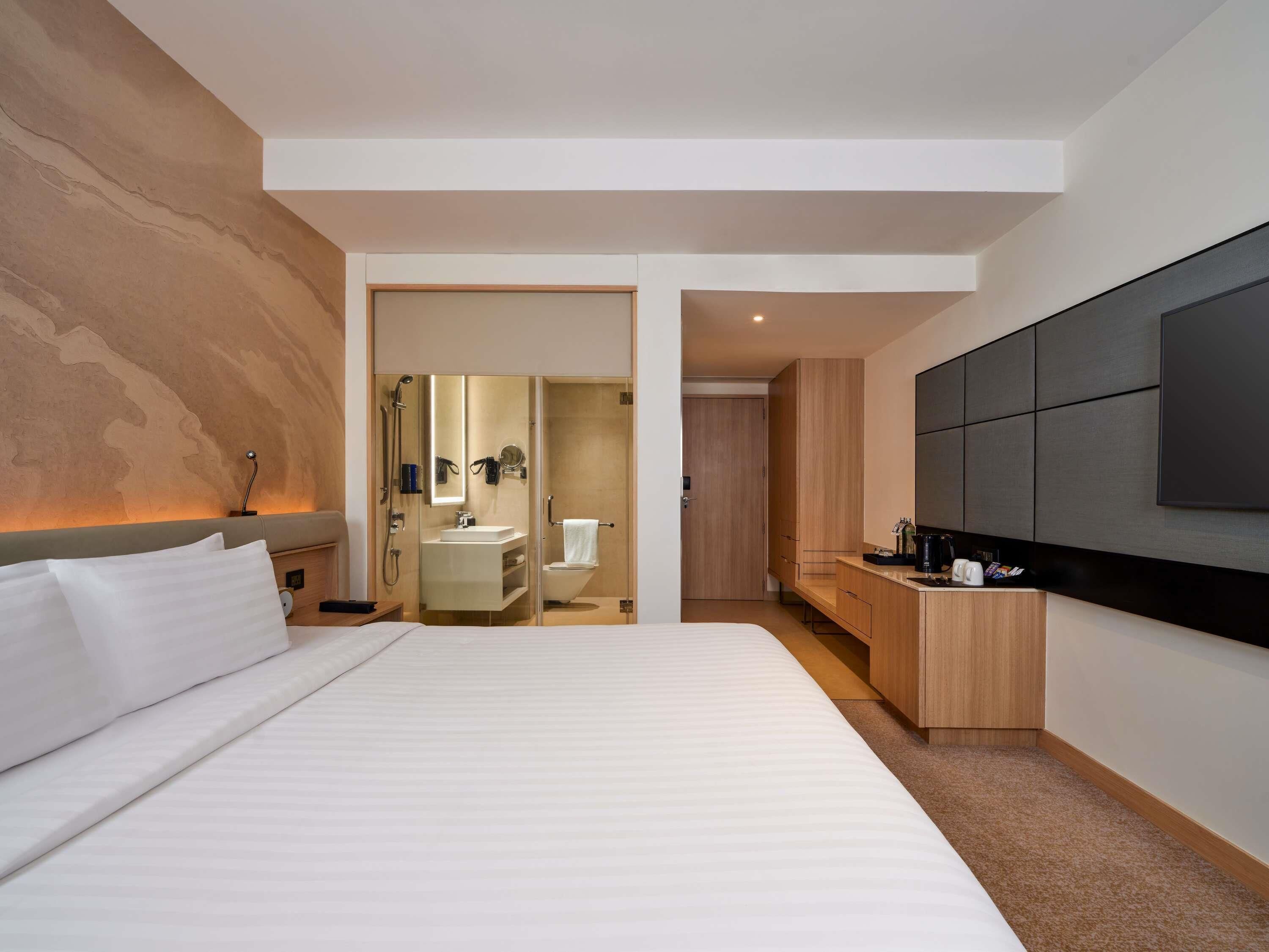 A modern hotel room with a large bed, a built-in desk, a large flat-screen TV, and a separate bathroom.