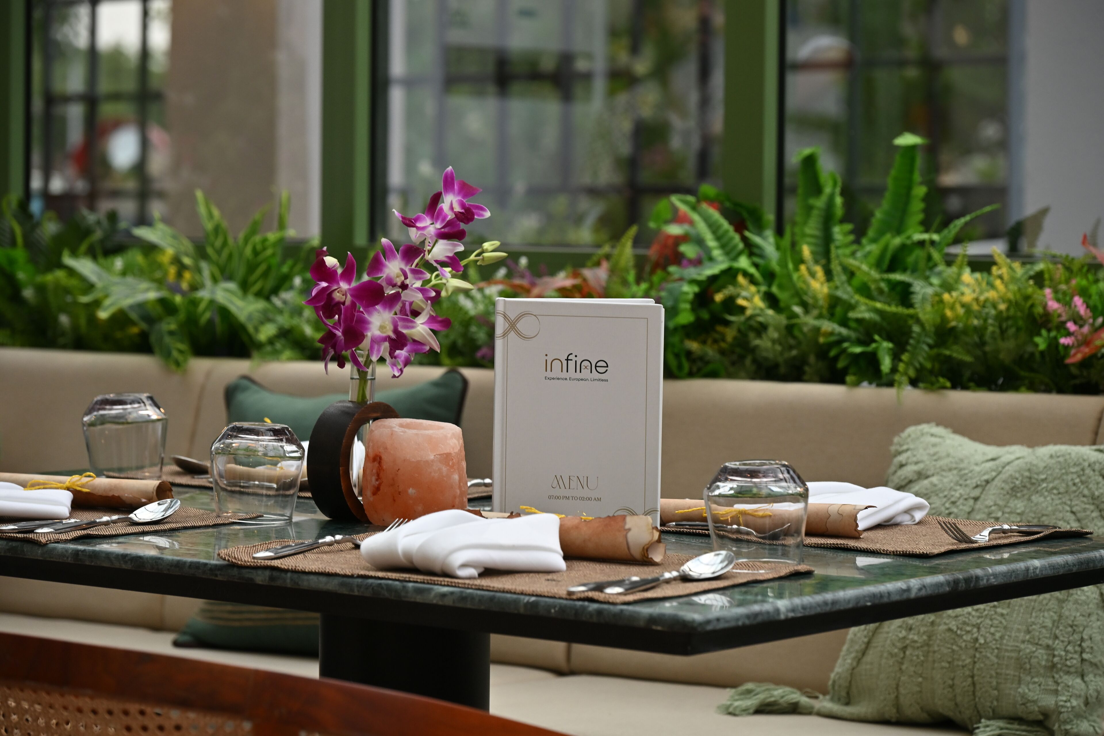A dining table set with a menu, a salt and pepper shaker, a candle, and a vase with purple flowers.