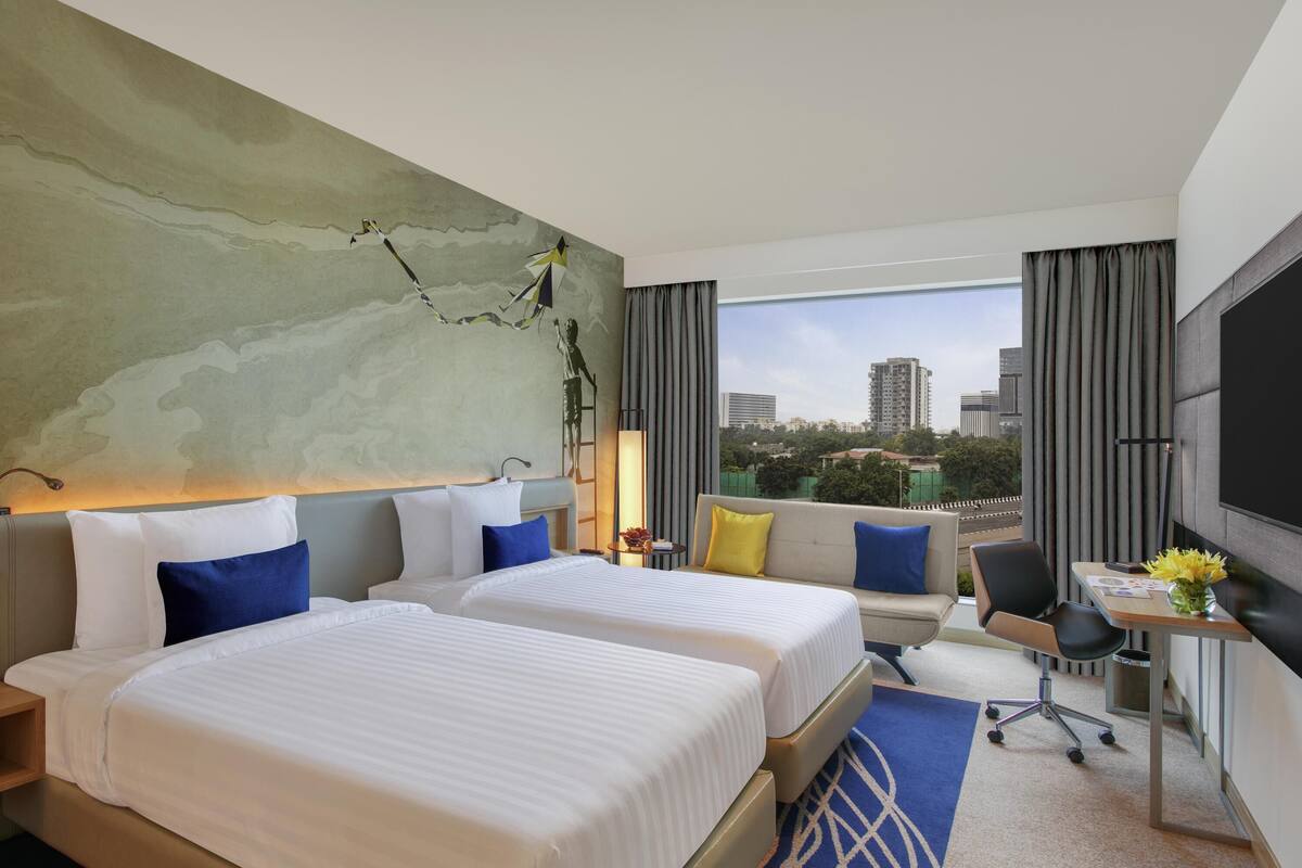 Une chambre d’hôtel avec deux lits, un canapé, un bureau et une grande fenêtre donnant sur la ville.