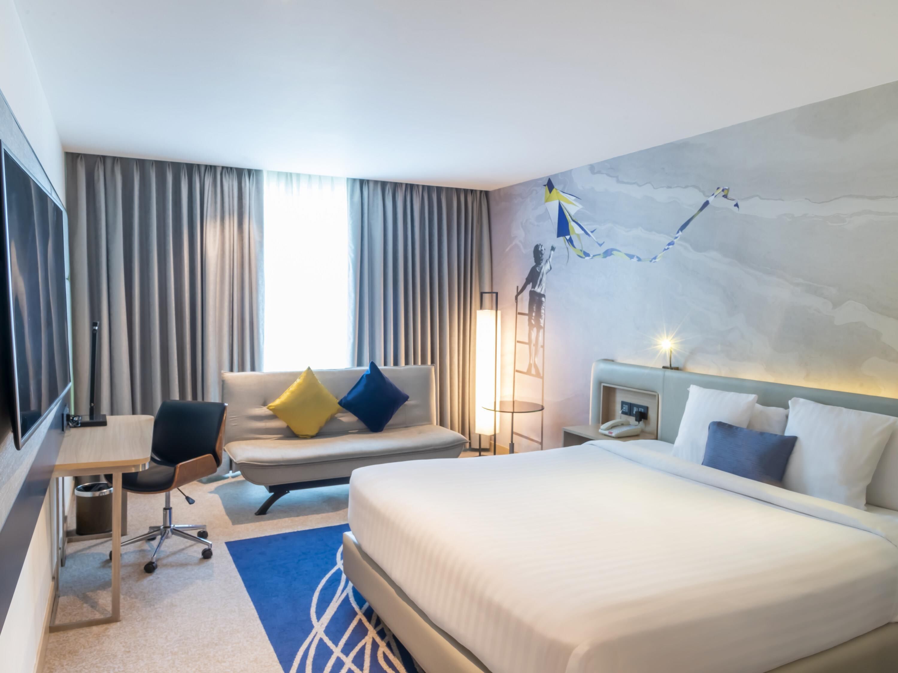 Et hotelværelse med en seng, et skrivebord, en stol, en lampe og en væg med et muralmaleri.