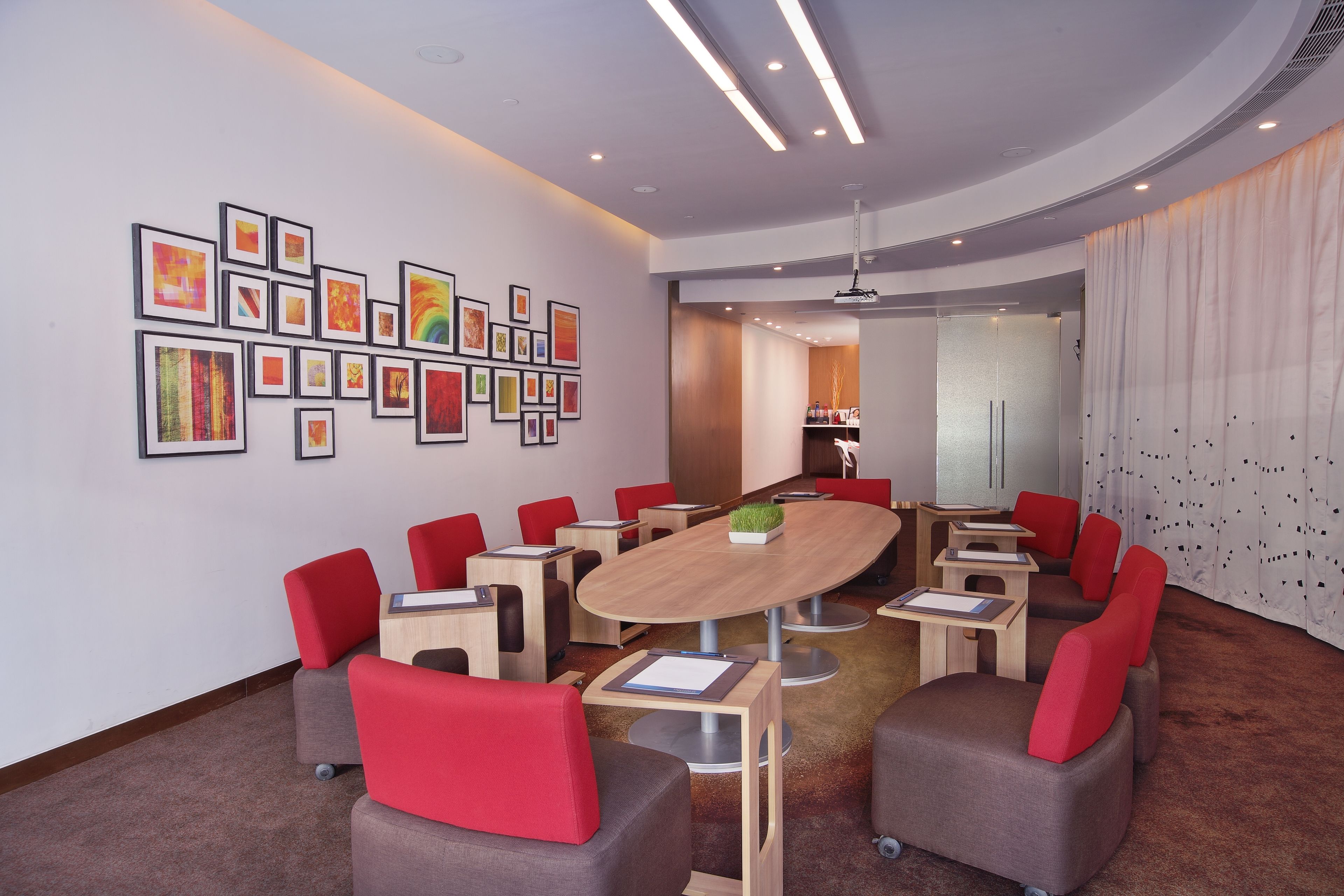 A conference room with a round table, red and grey chairs, and framed artwork on the walls.