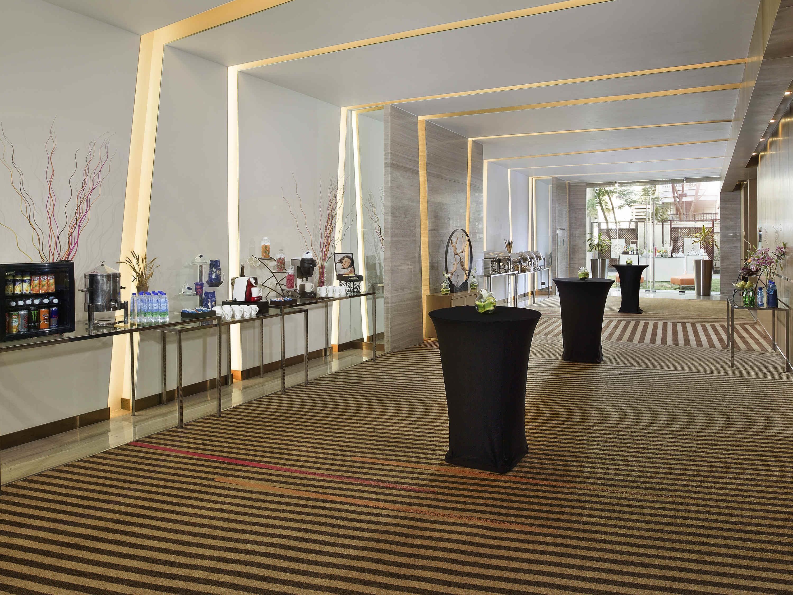 Una hall moderna di un hotel con reception, angolo caffè e piante in vaso.