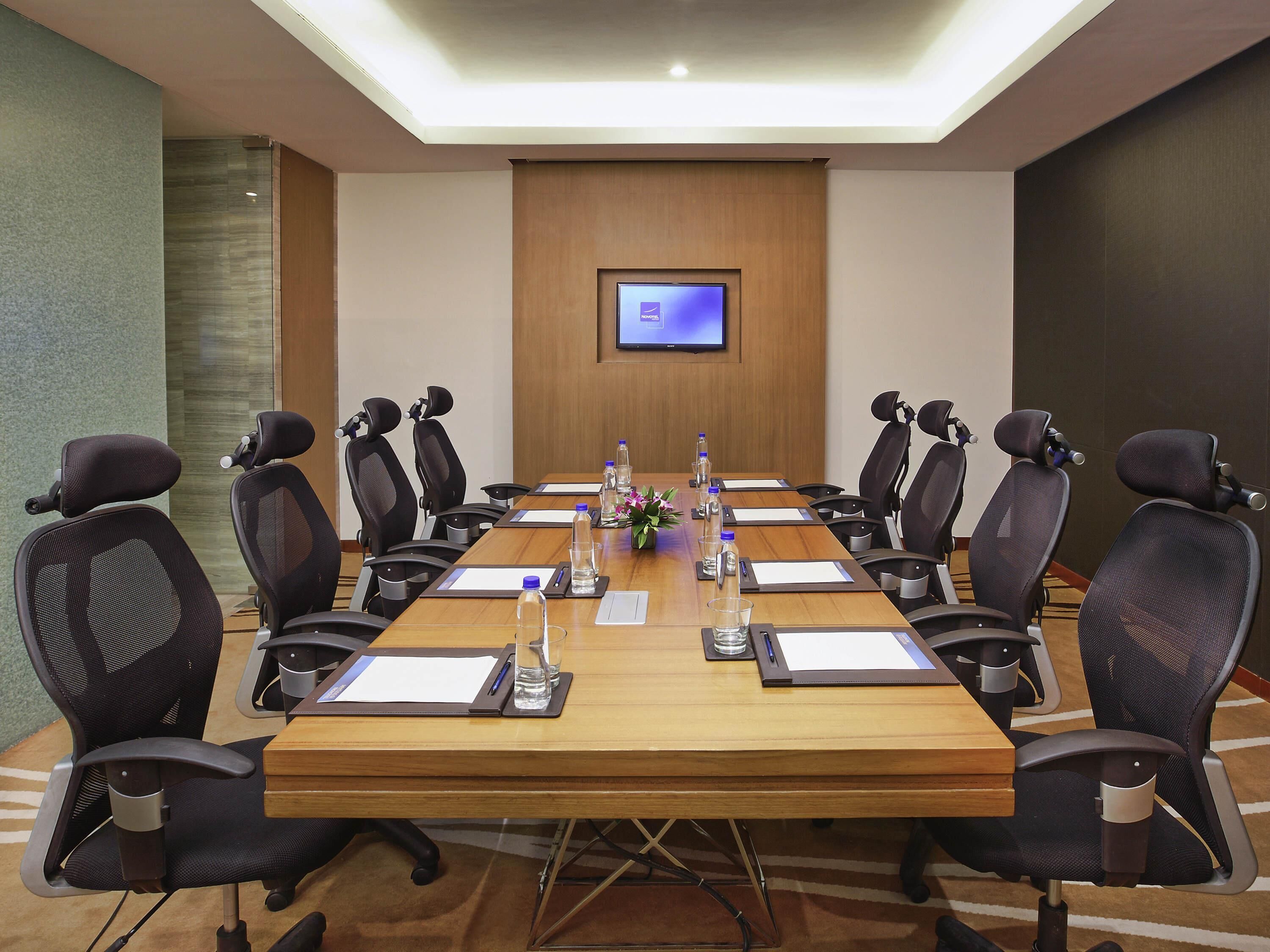 A conference room with a long table, chairs, a TV screen, and water bottles.