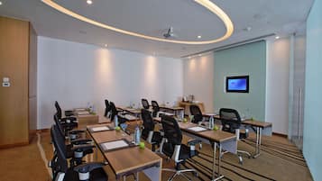 A conference room with multiple tables, chairs, and a television screen on the wall.