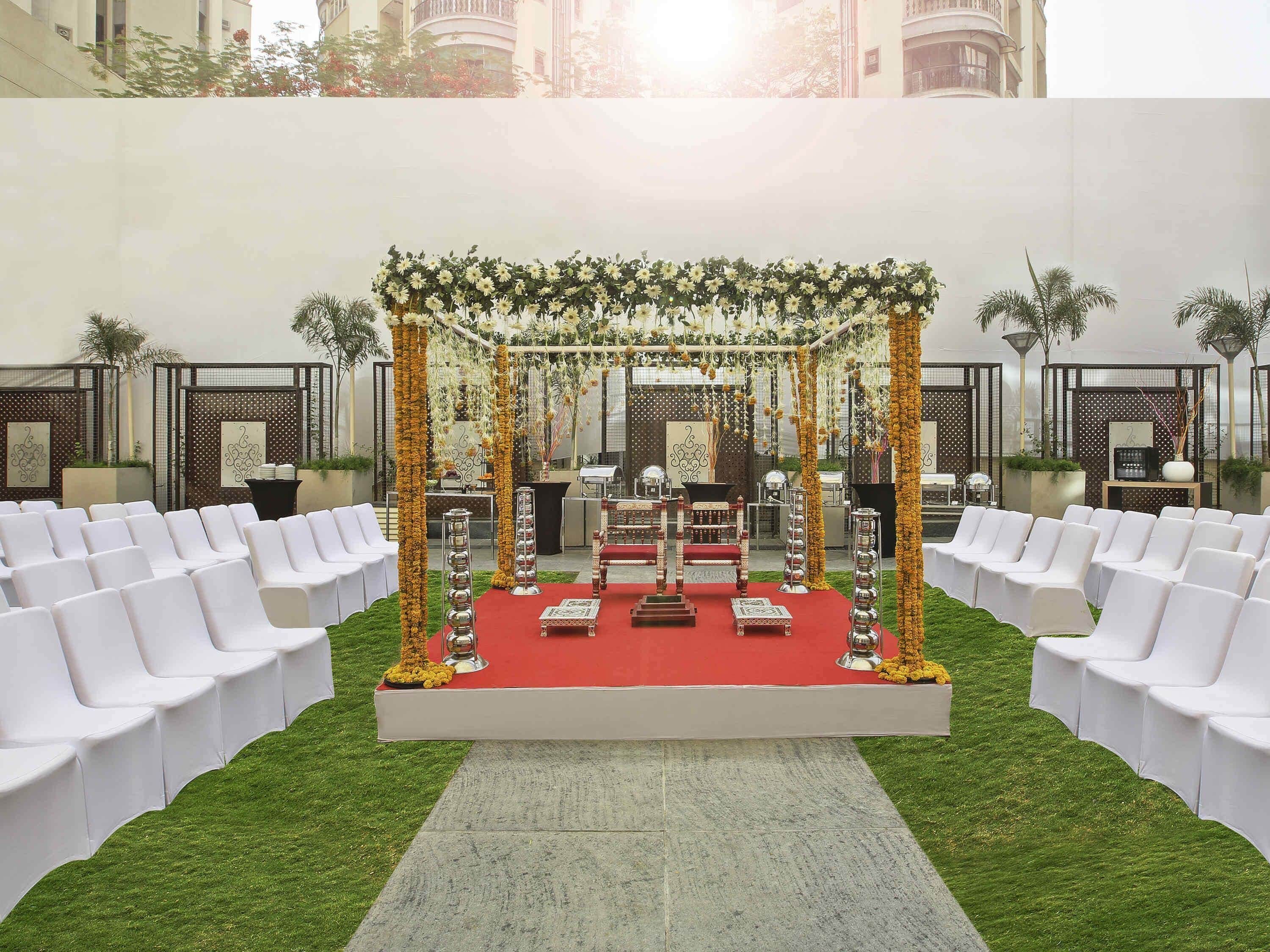 An outdoor wedding setup with a red carpet, white chairs, and a decorated stage.