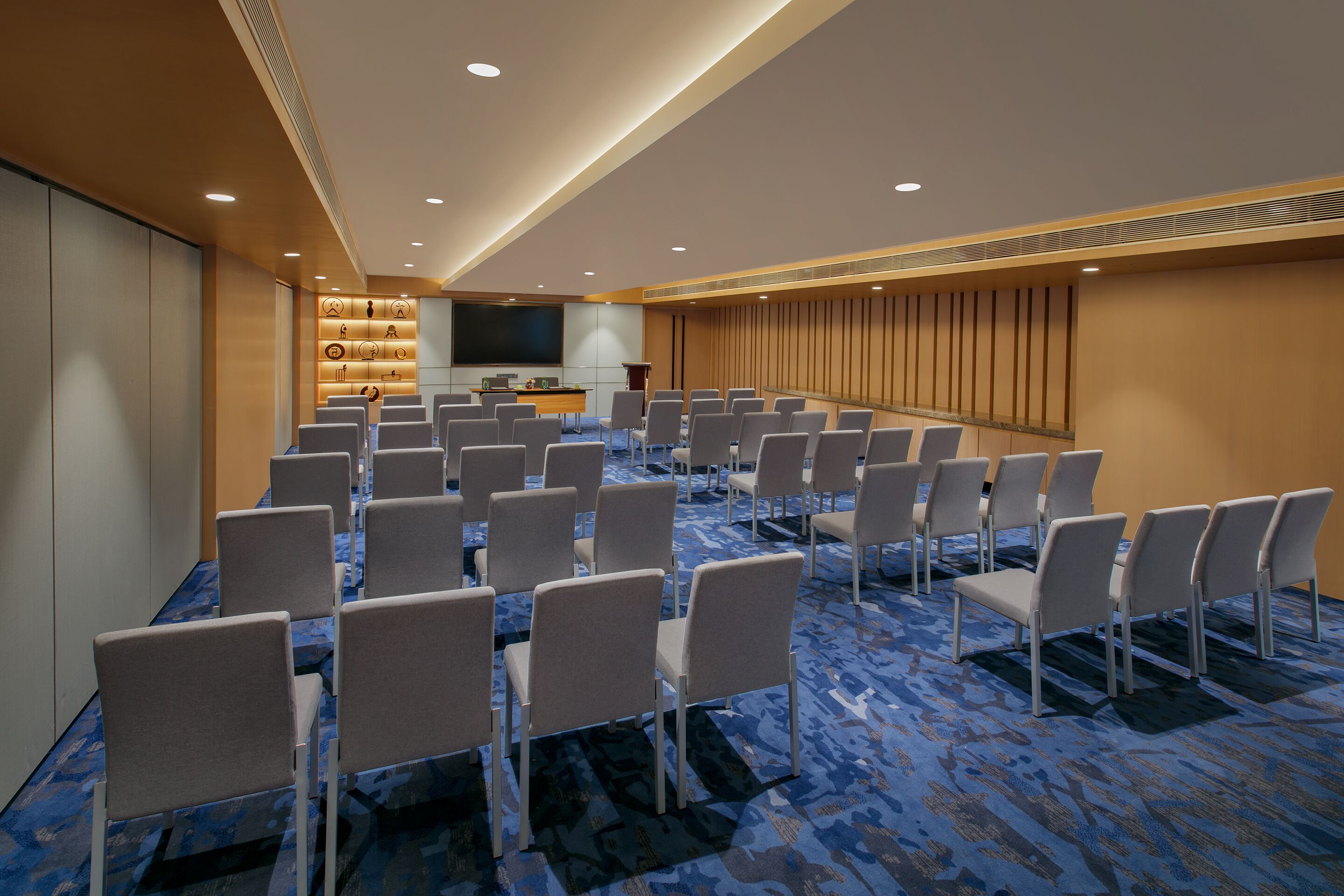 A conference room with rows of chairs, a podium, and a large screen.