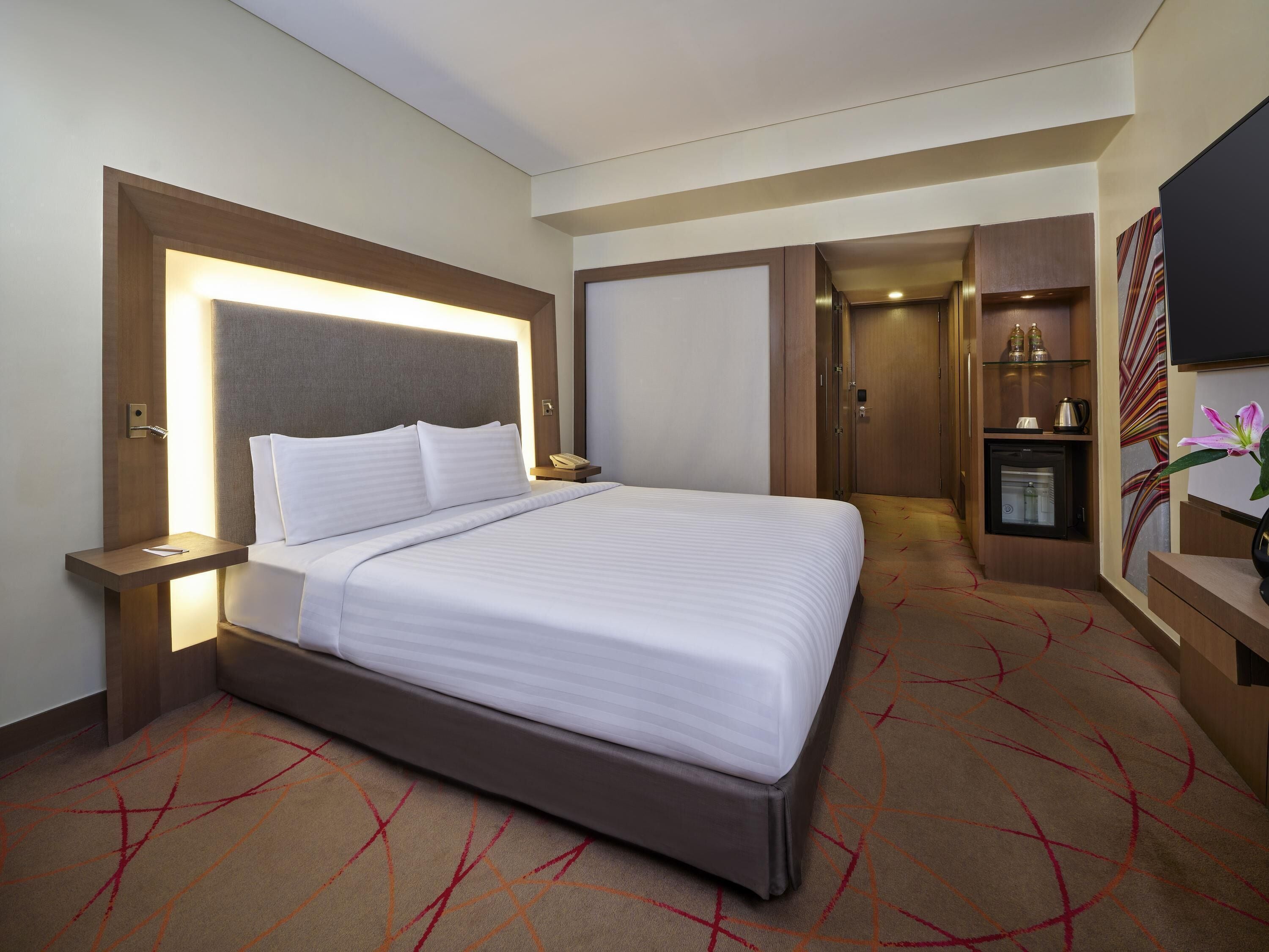 Une chambre d’hôtel comprenant un lit, des tables de chevet, un bureau, un mini-bar et une télévision.